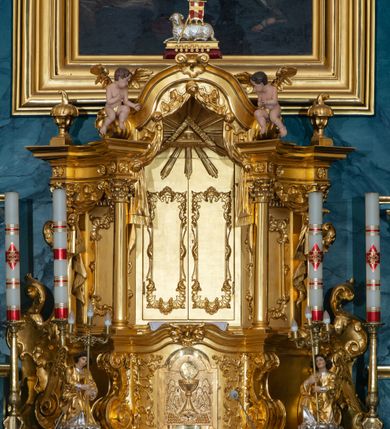 Zdjęcie nr 16: Ołtarz przyścienny, jednokondygnacyjny, jednoosiowy, ze zwieńczeniem. Ołtarz prostopadłościenny, tabernakulum z tronem wystawienia w formie architektonicznej na rzucie trapezoidalnym. W przedniej ściance wysokiego cokołu, o narożach ujętych spływami wolutowymi, są drzwiczki w kształcie prostokąta zamkniętego półkolistym łukiem nadwieszonym zdobione płaskorzeźbionym przedstawieniem kielicha eucharystycznego. Cokół wieńczy gzyms przekształcający się pośrodku w parę stykających się wolut. Na występach nad spływami cokołu osadzone kolumienki wspierające wyłamujące się ponad nimi belkowanie baldachimu tronu wystawienia. Zwieńczenie w formie pary stykających się spływów wolutowych z motywem paludamentu. Zaplecek zdobiony płycinami z ornamentalnymi obramieniami z motywami rocaille’u, w górnej partii płaskorzeźbiony trójkąt z okiem Opatrzności Bożej ujęty promienistą glorią. W zwieńczeniu para wazonów i para figurek aniołków, na szczycie księga z siedmioma pieczęciami i leżącym barankiem paschalnym.  
Retabulum osadzone na zdwojonym cokole, w górnej partii o zryzalitowanych bokach. Część środkową ujmują trzy pary kolumn, z których środkowe wysunięte, wspierających przerwane w partii architrawu i fryzu belkowanie. Zwieńczenie ujęte parą kolumn wspierających gzyms w formie trójkątnego przyczółka. Pola cokołu retabulum wypełnia stylizowana ornamentyka roślinna, partie fryzu oraz górne naroża części środkowej zdobią uskrzydlone główki anielskie, a gzyms kostkowanie. Zwieńczenie ujęte po bokach motywem liści paproci, pole ulistnionymi gałązkami z wstążką. Krawędź gzymsu wieńczącego zdobi wić roślinna z krzyżem pośrodku, po bokach para wazonów. Całość ujmuje para figur klęczących aniołów. Pole części środkowej w kształcie stojącego prostokąta ujętego profilowaną, złoconą ramą z przedstawieniem Narodzenia Najświętszej Marii Panny. W zwieńczeniu obraz w kształcie stojącego owalu, ujętego ramą zdobioną akantowymi liśćmi, z wizerunkiem św. Mikołaja. Struktura marmoryzowana w odcieniach błękitów, detal architektoniczny i ornamentyka złocone.   
