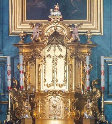 Zdjęcie nr 17: Ołtarz przyścienny, jednokondygnacyjny, jednoosiowy, ze zwieńczeniem. Ołtarz prostopadłościenny, tabernakulum z tronem wystawienia w formie architektonicznej na rzucie trapezoidalnym. W przedniej ściance wysokiego cokołu, o narożach ujętych spływami wolutowymi, są drzwiczki w kształcie prostokąta zamkniętego półkolistym łukiem nadwieszonym zdobione płaskorzeźbionym przedstawieniem kielicha eucharystycznego. Cokół wieńczy gzyms przekształcający się pośrodku w parę stykających się wolut. Na występach nad spływami cokołu osadzone kolumienki wspierające wyłamujące się ponad nimi belkowanie baldachimu tronu wystawienia. Zwieńczenie w formie pary stykających się spływów wolutowych z motywem paludamentu. Zaplecek zdobiony płycinami z ornamentalnymi obramieniami z motywami rocaille’u, w górnej partii płaskorzeźbiony trójkąt z okiem Opatrzności Bożej ujęty promienistą glorią. W zwieńczeniu para wazonów i para figurek aniołków, na szczycie księga z siedmioma pieczęciami i leżącym barankiem paschalnym.  
Retabulum osadzone na zdwojonym cokole, w górnej partii o zryzalitowanych bokach. Część środkową ujmują trzy pary kolumn, z których środkowe wysunięte, wspierających przerwane w partii architrawu i fryzu belkowanie. Zwieńczenie ujęte parą kolumn wspierających gzyms w formie trójkątnego przyczółka. Pola cokołu retabulum wypełnia stylizowana ornamentyka roślinna, partie fryzu oraz górne naroża części środkowej zdobią uskrzydlone główki anielskie, a gzyms kostkowanie. Zwieńczenie ujęte po bokach motywem liści paproci, pole ulistnionymi gałązkami z wstążką. Krawędź gzymsu wieńczącego zdobi wić roślinna z krzyżem pośrodku, po bokach para wazonów. Całość ujmuje para figur klęczących aniołów. Pole części środkowej w kształcie stojącego prostokąta ujętego profilowaną, złoconą ramą z przedstawieniem Narodzenia Najświętszej Marii Panny. W zwieńczeniu obraz w kształcie stojącego owalu, ujętego ramą zdobioną akantowymi liśćmi, z wizerunkiem św. Mikołaja. Struktura marmoryzowana w odcieniach błękitów, detal architektoniczny i ornamentyka złocone.   
