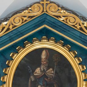 Zdjęcie nr 1: Obraz w kształcie stojącego owalu ujęty profilowaną, złoconą ramą o krawędzi zdobionej liśćmi akantu. Malowidło przedstawia reprezentacyjny, całopostaciowy wizerunek św. Mikołaja stojącego w lekkim kontrapoście i zwróconego na wprost. Skierowaną w trzech czwartych w prawo głowę charakteryzują rysy mężczyzny w podeszłym wieku, z długim, siwym zarostem. Święty Mikołaj jest ubrany w strój pontyfikalny składający się z ciemnoniebieskiej sutanny, rokiety, ciemnoniebieskiego mantoletu oraz białej kapy z czerwonym podszyciem, zdobionej złotym haftem. Na głowie ma białą infułę, na dłoniach niebieskie rękawiczki. Święty prawą rękę unosi w geście błogosławieństwa, w lewej, podtrzymując pastorał, ma zamkniętą księgę z leżącymi na niej trzema złotymi kulami. Postać ukazana jest na tle pejzażu z obniżoną linią horyzontu, po prawej stronie widoczne jest duże drzewo. Niebo pokrywają ciemne chmury, w lewej górnej części kompozycji widoczna jest wiązka promieni.     