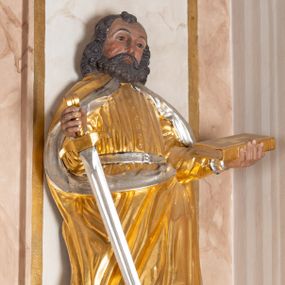 Zdjęcie nr 1: Całopostaciowa, drążona z tyłu figura św. Pawła stojącego na niewysokiej, ośmiobocznej podstawie. Święty zwrócony jest na wprost. Lekko przechyloną w lewo głowę charakteryzuje szeroka twarz o wyrazistych rysach z bruzdą na czole, mocno zarysowanymi łukami brwiowymi, prostym nosem, zaróżowionymi policzkami i bujnym, krótkim zarostem. Skręcone, ciemnobrązowe włosy, z kosmykiem nad czołem, sięgają ramion. Święty Paweł jest ubrany w długą, zapinaną na guziki złoconą suknię przewiązaną srebrzonym pasem, na ramiona ma narzucony spięty pod szyją, złocony płaszcz ze srebrzonym podszyciem, na stopach ciemnobrązowe, spiczaste buty. W zgiętych w łokciach, uniesionych na wysokości talii rękach trzyma miecz w prawej i zamkniętą, złocono-srebrzoną księgę w lewej.    