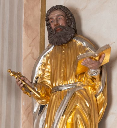 Zdjęcie nr 1: Całopostaciowa, drążona z tyłu figura św. Piotra stojącego na niewysokiej, ośmiobocznej podstawie. Święty zwrócony jest na wprost. Lekko przechyloną w prawo głowę charakteryzuje pociągła twarz o wyrazistych rysach z bruzdami na czole, mocno zarysowanymi łukami brwiowymi, wydatnym nosem i bujnym zarostem. Skręcone, ciemnobrązowe włosy sięgają ramion. Święty Piotr jest ubrany w długą, zapinaną na guziki, złoconą suknię przewiązaną srebrzonym pasem, na ramiona ma narzucony złocony płaszcz ze srebrzonym podszyciem, na stopach ciemnobrązowe, spiczaste buty. W zgiętych w łokciach, uniesionych na wysokości talii rękach ma parę złoconych kluczy – w prawej i otwartą, złocono-srebrzoną księgę – w lewej.    