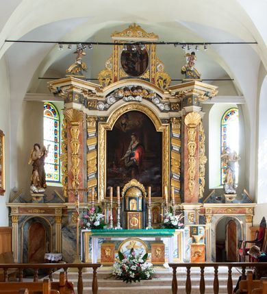 Zdjęcie nr 15: Świątynia otoczona jest murem kamiennym, tynkowanym, nakrytym daszkiem gontowym, jednospadowym. Wejścia znajdują się w murze od strony południowej. Pierwsze, prowadzące do głównych drzwi jest kamienną, późnobarokową bramką z herbem księdza Józefa Sawickiego, datą „1765” oraz figurą św. Jana Kantego. Drugie wejście prowadzi przez dzwonnicę. W murze, od strony wewnętrznej jest 14 wnęk po stacjach drogi krzyżowej. Teren wokół świątyni jest starym cmentarzem, bez zachowanych nagrobków.

Kościół jest budowlą założoną na planie prostokąta, orientowaną, jednonawową z ramionami w rodzaju krótkiego transeptu z wieżą od zachodu, zakrystią i kaplicą od północy oraz kruchtą od południa. Prezbiterium zamknięte jest wielobocznie, trójprzęsłowe, węższe i niższe od nawy. Nawa czteroprzęsłowa, nie jest ulokowana na jednej osi z prezbiterium. 

Artykulacja ścian jest przeprowadzona za pomocą pilastrów toskańskich podtrzymujących sklepienie kolebkowe z lunetami. Ramiona transeptu, kaplica Matki Boskiej Różańcowej oraz kruchta są sklepione krzyżowo. Otwory okienne: w prezbiterium cztery, w nawie cztery od południa, wszystkie zamknięte łukami półkolistymi. Zakrystia piętrowa z jednym oknem na parterze i dwoma na piętrze; od strony północnej kaplica Matki Boskiej Różańcowej z dwoma oknami i jedną, zamurowaną wnęką; obok mała zakrystia. Z prezbiterium do zakrystii prowadzi portal kamienny z inicjałami, herbem i portretem księdza Sawickiego. Na arkadzie tęczowej od strony nawy nowy napis: „FUNDATA A CASIMIRO MAGNO ANNO DOM[INI] 1346”. W pierwszym od strony fasady przęśle znajduje się drewniany chór muzyczny, wsparty na dwóch filarach.

Fasada zachodnia kościoła jest płaska z wieżą, nakryta kopułą z latarnią. Na narożnikach zewnętrznych wieży i naw oraz przy absydzie szkarpy, kryte daszkiem gontowym. Na frontowej ścianie wieży kamienny portal, nad nim sygle „I(osephus) S(awicki) / 1765” oraz herb Nowina. Od strony zachodniej wieża, ozdobiona półkolistymi blendami. Od strony południowej balkonik otoczony żelazną kratą z napisem „1343-1943”. Nad balkonikiem umieszczona jest tarcza zegara, taka sama widnieje od strony północnej, a od zachodniej i wschodniej odpowiadają im tarcze w murze. Przy wieży, od strony północnej wieżyczka w kształcie walca, ścięta od połowy, nakryta daszkiem stożkowym. Przy południowej ścianie wieży między dwiema szkarpami znajduje się kapliczka Ukrzyżowania z figurami Chrystusa Ukrzyżowanego i dwóch łotrów na krzyżach. Dach kościoła siodłowy, kryty gontem.

Na zewnętrznej, południowej ścianie napis: „AEDIFICATA H(A)EC EC[C]LESIA / A[NNO] D[OMINI] / 1606 / PETRVS CZARNY MVLARS”. Niżej wmurowana w półokrągłą wnękę z piaskowca figura Matki Boskiej Niepokalanie Poczętej. Po lewej stronie, u góry fragment fryzu dekoracyjnego, malowany w kolorze czerwonym o motywie zwisających esownic ze stylizowanymi kwiatami i liliami. 

Dzwonnica na planie kwadratu, murowana, otynkowana, dwupiętrowa z sienią przejściową sklepioną, ujętą na zaokrąglonych narożnikach zdwojonymi pilastrami; nakryta gontowym hełmem. Na osi dzwonnicy portal bramy flankowany dwoma pilastrami, o spłaszczonej archiwolcie. Nad belkowaniem monogram maryjny i data „1701”. W sieni na ścianie wschodniej barokowy krucyfiks oraz rzeźby Matki Boskiej i św. Jana Ewangelisty, na ścianie pozostałości polichromii z XVIII wieku.
