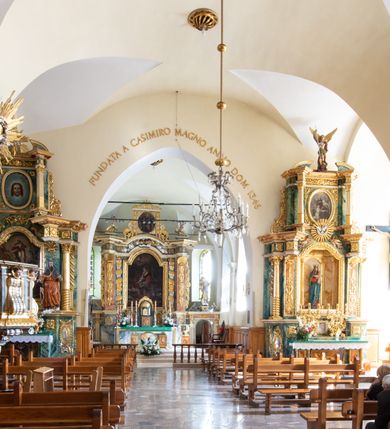 Zdjęcie nr 13: Świątynia otoczona jest murem kamiennym, tynkowanym, nakrytym daszkiem gontowym, jednospadowym. Wejścia znajdują się w murze od strony południowej. Pierwsze, prowadzące do głównych drzwi jest kamienną, późnobarokową bramką z herbem księdza Józefa Sawickiego, datą „1765” oraz figurą św. Jana Kantego. Drugie wejście prowadzi przez dzwonnicę. W murze, od strony wewnętrznej jest 14 wnęk po stacjach drogi krzyżowej. Teren wokół świątyni jest starym cmentarzem, bez zachowanych nagrobków.

Kościół jest budowlą założoną na planie prostokąta, orientowaną, jednonawową z ramionami w rodzaju krótkiego transeptu z wieżą od zachodu, zakrystią i kaplicą od północy oraz kruchtą od południa. Prezbiterium zamknięte jest wielobocznie, trójprzęsłowe, węższe i niższe od nawy. Nawa czteroprzęsłowa, nie jest ulokowana na jednej osi z prezbiterium. 

Artykulacja ścian jest przeprowadzona za pomocą pilastrów toskańskich podtrzymujących sklepienie kolebkowe z lunetami. Ramiona transeptu, kaplica Matki Boskiej Różańcowej oraz kruchta są sklepione krzyżowo. Otwory okienne: w prezbiterium cztery, w nawie cztery od południa, wszystkie zamknięte łukami półkolistymi. Zakrystia piętrowa z jednym oknem na parterze i dwoma na piętrze; od strony północnej kaplica Matki Boskiej Różańcowej z dwoma oknami i jedną, zamurowaną wnęką; obok mała zakrystia. Z prezbiterium do zakrystii prowadzi portal kamienny z inicjałami, herbem i portretem księdza Sawickiego. Na arkadzie tęczowej od strony nawy nowy napis: „FUNDATA A CASIMIRO MAGNO ANNO DOM[INI] 1346”. W pierwszym od strony fasady przęśle znajduje się drewniany chór muzyczny, wsparty na dwóch filarach.

Fasada zachodnia kościoła jest płaska z wieżą, nakryta kopułą z latarnią. Na narożnikach zewnętrznych wieży i naw oraz przy absydzie szkarpy, kryte daszkiem gontowym. Na frontowej ścianie wieży kamienny portal, nad nim sygle „I(osephus) S(awicki) / 1765” oraz herb Nowina. Od strony zachodniej wieża, ozdobiona półkolistymi blendami. Od strony południowej balkonik otoczony żelazną kratą z napisem „1343-1943”. Nad balkonikiem umieszczona jest tarcza zegara, taka sama widnieje od strony północnej, a od zachodniej i wschodniej odpowiadają im tarcze w murze. Przy wieży, od strony północnej wieżyczka w kształcie walca, ścięta od połowy, nakryta daszkiem stożkowym. Przy południowej ścianie wieży między dwiema szkarpami znajduje się kapliczka Ukrzyżowania z figurami Chrystusa Ukrzyżowanego i dwóch łotrów na krzyżach. Dach kościoła siodłowy, kryty gontem.

Na zewnętrznej, południowej ścianie napis: „AEDIFICATA H(A)EC EC[C]LESIA / A[NNO] D[OMINI] / 1606 / PETRVS CZARNY MVLARS”. Niżej wmurowana w półokrągłą wnękę z piaskowca figura Matki Boskiej Niepokalanie Poczętej. Po lewej stronie, u góry fragment fryzu dekoracyjnego, malowany w kolorze czerwonym o motywie zwisających esownic ze stylizowanymi kwiatami i liliami. 

Dzwonnica na planie kwadratu, murowana, otynkowana, dwupiętrowa z sienią przejściową sklepioną, ujętą na zaokrąglonych narożnikach zdwojonymi pilastrami; nakryta gontowym hełmem. Na osi dzwonnicy portal bramy flankowany dwoma pilastrami, o spłaszczonej archiwolcie. Nad belkowaniem monogram maryjny i data „1701”. W sieni na ścianie wschodniej barokowy krucyfiks oraz rzeźby Matki Boskiej i św. Jana Ewangelisty, na ścianie pozostałości polichromii z XVIII wieku.
