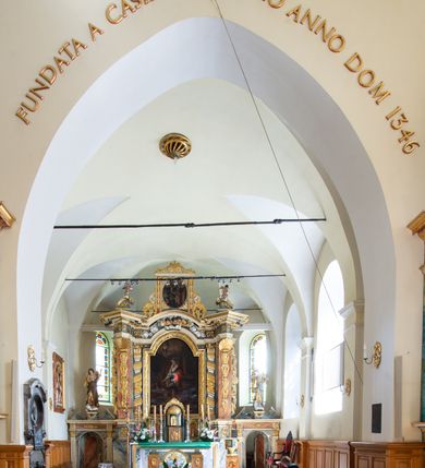 Zdjęcie nr 16: Świątynia otoczona jest murem kamiennym, tynkowanym, nakrytym daszkiem gontowym, jednospadowym. Wejścia znajdują się w murze od strony południowej. Pierwsze, prowadzące do głównych drzwi jest kamienną, późnobarokową bramką z herbem księdza Józefa Sawickiego, datą „1765” oraz figurą św. Jana Kantego. Drugie wejście prowadzi przez dzwonnicę. W murze, od strony wewnętrznej jest 14 wnęk po stacjach drogi krzyżowej. Teren wokół świątyni jest starym cmentarzem, bez zachowanych nagrobków.

Kościół jest budowlą założoną na planie prostokąta, orientowaną, jednonawową z ramionami w rodzaju krótkiego transeptu z wieżą od zachodu, zakrystią i kaplicą od północy oraz kruchtą od południa. Prezbiterium zamknięte jest wielobocznie, trójprzęsłowe, węższe i niższe od nawy. Nawa czteroprzęsłowa, nie jest ulokowana na jednej osi z prezbiterium. 

Artykulacja ścian jest przeprowadzona za pomocą pilastrów toskańskich podtrzymujących sklepienie kolebkowe z lunetami. Ramiona transeptu, kaplica Matki Boskiej Różańcowej oraz kruchta są sklepione krzyżowo. Otwory okienne: w prezbiterium cztery, w nawie cztery od południa, wszystkie zamknięte łukami półkolistymi. Zakrystia piętrowa z jednym oknem na parterze i dwoma na piętrze; od strony północnej kaplica Matki Boskiej Różańcowej z dwoma oknami i jedną, zamurowaną wnęką; obok mała zakrystia. Z prezbiterium do zakrystii prowadzi portal kamienny z inicjałami, herbem i portretem księdza Sawickiego. Na arkadzie tęczowej od strony nawy nowy napis: „FUNDATA A CASIMIRO MAGNO ANNO DOM[INI] 1346”. W pierwszym od strony fasady przęśle znajduje się drewniany chór muzyczny, wsparty na dwóch filarach.

Fasada zachodnia kościoła jest płaska z wieżą, nakryta kopułą z latarnią. Na narożnikach zewnętrznych wieży i naw oraz przy absydzie szkarpy, kryte daszkiem gontowym. Na frontowej ścianie wieży kamienny portal, nad nim sygle „I(osephus) S(awicki) / 1765” oraz herb Nowina. Od strony zachodniej wieża, ozdobiona półkolistymi blendami. Od strony południowej balkonik otoczony żelazną kratą z napisem „1343-1943”. Nad balkonikiem umieszczona jest tarcza zegara, taka sama widnieje od strony północnej, a od zachodniej i wschodniej odpowiadają im tarcze w murze. Przy wieży, od strony północnej wieżyczka w kształcie walca, ścięta od połowy, nakryta daszkiem stożkowym. Przy południowej ścianie wieży między dwiema szkarpami znajduje się kapliczka Ukrzyżowania z figurami Chrystusa Ukrzyżowanego i dwóch łotrów na krzyżach. Dach kościoła siodłowy, kryty gontem.

Na zewnętrznej, południowej ścianie napis: „AEDIFICATA H(A)EC EC[C]LESIA / A[NNO] D[OMINI] / 1606 / PETRVS CZARNY MVLARS”. Niżej wmurowana w półokrągłą wnękę z piaskowca figura Matki Boskiej Niepokalanie Poczętej. Po lewej stronie, u góry fragment fryzu dekoracyjnego, malowany w kolorze czerwonym o motywie zwisających esownic ze stylizowanymi kwiatami i liliami. 

Dzwonnica na planie kwadratu, murowana, otynkowana, dwupiętrowa z sienią przejściową sklepioną, ujętą na zaokrąglonych narożnikach zdwojonymi pilastrami; nakryta gontowym hełmem. Na osi dzwonnicy portal bramy flankowany dwoma pilastrami, o spłaszczonej archiwolcie. Nad belkowaniem monogram maryjny i data „1701”. W sieni na ścianie wschodniej barokowy krucyfiks oraz rzeźby Matki Boskiej i św. Jana Ewangelisty, na ścianie pozostałości polichromii z XVIII wieku.
