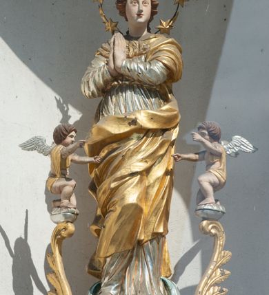Zdjęcie nr 10: Świątynia otoczona jest murem kamiennym, tynkowanym, nakrytym daszkiem gontowym, jednospadowym. Wejścia znajdują się w murze od strony południowej. Pierwsze, prowadzące do głównych drzwi jest kamienną, późnobarokową bramką z herbem księdza Józefa Sawickiego, datą „1765” oraz figurą św. Jana Kantego. Drugie wejście prowadzi przez dzwonnicę. W murze, od strony wewnętrznej jest 14 wnęk po stacjach drogi krzyżowej. Teren wokół świątyni jest starym cmentarzem, bez zachowanych nagrobków.

Kościół jest budowlą założoną na planie prostokąta, orientowaną, jednonawową z ramionami w rodzaju krótkiego transeptu z wieżą od zachodu, zakrystią i kaplicą od północy oraz kruchtą od południa. Prezbiterium zamknięte jest wielobocznie, trójprzęsłowe, węższe i niższe od nawy. Nawa czteroprzęsłowa, nie jest ulokowana na jednej osi z prezbiterium. 

Artykulacja ścian jest przeprowadzona za pomocą pilastrów toskańskich podtrzymujących sklepienie kolebkowe z lunetami. Ramiona transeptu, kaplica Matki Boskiej Różańcowej oraz kruchta są sklepione krzyżowo. Otwory okienne: w prezbiterium cztery, w nawie cztery od południa, wszystkie zamknięte łukami półkolistymi. Zakrystia piętrowa z jednym oknem na parterze i dwoma na piętrze; od strony północnej kaplica Matki Boskiej Różańcowej z dwoma oknami i jedną, zamurowaną wnęką; obok mała zakrystia. Z prezbiterium do zakrystii prowadzi portal kamienny z inicjałami, herbem i portretem księdza Sawickiego. Na arkadzie tęczowej od strony nawy nowy napis: „FUNDATA A CASIMIRO MAGNO ANNO DOM[INI] 1346”. W pierwszym od strony fasady przęśle znajduje się drewniany chór muzyczny, wsparty na dwóch filarach.

Fasada zachodnia kościoła jest płaska z wieżą, nakryta kopułą z latarnią. Na narożnikach zewnętrznych wieży i naw oraz przy absydzie szkarpy, kryte daszkiem gontowym. Na frontowej ścianie wieży kamienny portal, nad nim sygle „I(osephus) S(awicki) / 1765” oraz herb Nowina. Od strony zachodniej wieża, ozdobiona półkolistymi blendami. Od strony południowej balkonik otoczony żelazną kratą z napisem „1343-1943”. Nad balkonikiem umieszczona jest tarcza zegara, taka sama widnieje od strony północnej, a od zachodniej i wschodniej odpowiadają im tarcze w murze. Przy wieży, od strony północnej wieżyczka w kształcie walca, ścięta od połowy, nakryta daszkiem stożkowym. Przy południowej ścianie wieży między dwiema szkarpami znajduje się kapliczka Ukrzyżowania z figurami Chrystusa Ukrzyżowanego i dwóch łotrów na krzyżach. Dach kościoła siodłowy, kryty gontem.

Na zewnętrznej, południowej ścianie napis: „AEDIFICATA H(A)EC EC[C]LESIA / A[NNO] D[OMINI] / 1606 / PETRVS CZARNY MVLARS”. Niżej wmurowana w półokrągłą wnękę z piaskowca figura Matki Boskiej Niepokalanie Poczętej. Po lewej stronie, u góry fragment fryzu dekoracyjnego, malowany w kolorze czerwonym o motywie zwisających esownic ze stylizowanymi kwiatami i liliami. 

Dzwonnica na planie kwadratu, murowana, otynkowana, dwupiętrowa z sienią przejściową sklepioną, ujętą na zaokrąglonych narożnikach zdwojonymi pilastrami; nakryta gontowym hełmem. Na osi dzwonnicy portal bramy flankowany dwoma pilastrami, o spłaszczonej archiwolcie. Nad belkowaniem monogram maryjny i data „1701”. W sieni na ścianie wschodniej barokowy krucyfiks oraz rzeźby Matki Boskiej i św. Jana Ewangelisty, na ścianie pozostałości polichromii z XVIII wieku.
