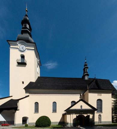 Zdjęcie nr 2: Świątynia otoczona jest murem kamiennym, tynkowanym, nakrytym daszkiem gontowym, jednospadowym. Wejścia znajdują się w murze od strony południowej. Pierwsze, prowadzące do głównych drzwi jest kamienną, późnobarokową bramką z herbem księdza Józefa Sawickiego, datą „1765” oraz figurą św. Jana Kantego. Drugie wejście prowadzi przez dzwonnicę. W murze, od strony wewnętrznej jest 14 wnęk po stacjach drogi krzyżowej. Teren wokół świątyni jest starym cmentarzem, bez zachowanych nagrobków.

Kościół jest budowlą założoną na planie prostokąta, orientowaną, jednonawową z ramionami w rodzaju krótkiego transeptu z wieżą od zachodu, zakrystią i kaplicą od północy oraz kruchtą od południa. Prezbiterium zamknięte jest wielobocznie, trójprzęsłowe, węższe i niższe od nawy. Nawa czteroprzęsłowa, nie jest ulokowana na jednej osi z prezbiterium. 

Artykulacja ścian jest przeprowadzona za pomocą pilastrów toskańskich podtrzymujących sklepienie kolebkowe z lunetami. Ramiona transeptu, kaplica Matki Boskiej Różańcowej oraz kruchta są sklepione krzyżowo. Otwory okienne: w prezbiterium cztery, w nawie cztery od południa, wszystkie zamknięte łukami półkolistymi. Zakrystia piętrowa z jednym oknem na parterze i dwoma na piętrze; od strony północnej kaplica Matki Boskiej Różańcowej z dwoma oknami i jedną, zamurowaną wnęką; obok mała zakrystia. Z prezbiterium do zakrystii prowadzi portal kamienny z inicjałami, herbem i portretem księdza Sawickiego. Na arkadzie tęczowej od strony nawy nowy napis: „FUNDATA A CASIMIRO MAGNO ANNO DOM[INI] 1346”. W pierwszym od strony fasady przęśle znajduje się drewniany chór muzyczny, wsparty na dwóch filarach.

Fasada zachodnia kościoła jest płaska z wieżą, nakryta kopułą z latarnią. Na narożnikach zewnętrznych wieży i naw oraz przy absydzie szkarpy, kryte daszkiem gontowym. Na frontowej ścianie wieży kamienny portal, nad nim sygle „I(osephus) S(awicki) / 1765” oraz herb Nowina. Od strony zachodniej wieża, ozdobiona półkolistymi blendami. Od strony południowej balkonik otoczony żelazną kratą z napisem „1343-1943”. Nad balkonikiem umieszczona jest tarcza zegara, taka sama widnieje od strony północnej, a od zachodniej i wschodniej odpowiadają im tarcze w murze. Przy wieży, od strony północnej wieżyczka w kształcie walca, ścięta od połowy, nakryta daszkiem stożkowym. Przy południowej ścianie wieży między dwiema szkarpami znajduje się kapliczka Ukrzyżowania z figurami Chrystusa Ukrzyżowanego i dwóch łotrów na krzyżach. Dach kościoła siodłowy, kryty gontem.

Na zewnętrznej, południowej ścianie napis: „AEDIFICATA H(A)EC EC[C]LESIA / A[NNO] D[OMINI] / 1606 / PETRVS CZARNY MVLARS”. Niżej wmurowana w półokrągłą wnękę z piaskowca figura Matki Boskiej Niepokalanie Poczętej. Po lewej stronie, u góry fragment fryzu dekoracyjnego, malowany w kolorze czerwonym o motywie zwisających esownic ze stylizowanymi kwiatami i liliami. 

Dzwonnica na planie kwadratu, murowana, otynkowana, dwupiętrowa z sienią przejściową sklepioną, ujętą na zaokrąglonych narożnikach zdwojonymi pilastrami; nakryta gontowym hełmem. Na osi dzwonnicy portal bramy flankowany dwoma pilastrami, o spłaszczonej archiwolcie. Nad belkowaniem monogram maryjny i data „1701”. W sieni na ścianie wschodniej barokowy krucyfiks oraz rzeźby Matki Boskiej i św. Jana Ewangelisty, na ścianie pozostałości polichromii z XVIII wieku.
