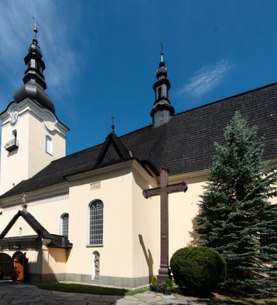 Zdjęcie nr 4: Świątynia otoczona jest murem kamiennym, tynkowanym, nakrytym daszkiem gontowym, jednospadowym. Wejścia znajdują się w murze od strony południowej. Pierwsze, prowadzące do głównych drzwi jest kamienną, późnobarokową bramką z herbem księdza Józefa Sawickiego, datą „1765” oraz figurą św. Jana Kantego. Drugie wejście prowadzi przez dzwonnicę. W murze, od strony wewnętrznej jest 14 wnęk po stacjach drogi krzyżowej. Teren wokół świątyni jest starym cmentarzem, bez zachowanych nagrobków.

Kościół jest budowlą założoną na planie prostokąta, orientowaną, jednonawową z ramionami w rodzaju krótkiego transeptu z wieżą od zachodu, zakrystią i kaplicą od północy oraz kruchtą od południa. Prezbiterium zamknięte jest wielobocznie, trójprzęsłowe, węższe i niższe od nawy. Nawa czteroprzęsłowa, nie jest ulokowana na jednej osi z prezbiterium. 

Artykulacja ścian jest przeprowadzona za pomocą pilastrów toskańskich podtrzymujących sklepienie kolebkowe z lunetami. Ramiona transeptu, kaplica Matki Boskiej Różańcowej oraz kruchta są sklepione krzyżowo. Otwory okienne: w prezbiterium cztery, w nawie cztery od południa, wszystkie zamknięte łukami półkolistymi. Zakrystia piętrowa z jednym oknem na parterze i dwoma na piętrze; od strony północnej kaplica Matki Boskiej Różańcowej z dwoma oknami i jedną, zamurowaną wnęką; obok mała zakrystia. Z prezbiterium do zakrystii prowadzi portal kamienny z inicjałami, herbem i portretem księdza Sawickiego. Na arkadzie tęczowej od strony nawy nowy napis: „FUNDATA A CASIMIRO MAGNO ANNO DOM[INI] 1346”. W pierwszym od strony fasady przęśle znajduje się drewniany chór muzyczny, wsparty na dwóch filarach.

Fasada zachodnia kościoła jest płaska z wieżą, nakryta kopułą z latarnią. Na narożnikach zewnętrznych wieży i naw oraz przy absydzie szkarpy, kryte daszkiem gontowym. Na frontowej ścianie wieży kamienny portal, nad nim sygle „I(osephus) S(awicki) / 1765” oraz herb Nowina. Od strony zachodniej wieża, ozdobiona półkolistymi blendami. Od strony południowej balkonik otoczony żelazną kratą z napisem „1343-1943”. Nad balkonikiem umieszczona jest tarcza zegara, taka sama widnieje od strony północnej, a od zachodniej i wschodniej odpowiadają im tarcze w murze. Przy wieży, od strony północnej wieżyczka w kształcie walca, ścięta od połowy, nakryta daszkiem stożkowym. Przy południowej ścianie wieży między dwiema szkarpami znajduje się kapliczka Ukrzyżowania z figurami Chrystusa Ukrzyżowanego i dwóch łotrów na krzyżach. Dach kościoła siodłowy, kryty gontem.

Na zewnętrznej, południowej ścianie napis: „AEDIFICATA H(A)EC EC[C]LESIA / A[NNO] D[OMINI] / 1606 / PETRVS CZARNY MVLARS”. Niżej wmurowana w półokrągłą wnękę z piaskowca figura Matki Boskiej Niepokalanie Poczętej. Po lewej stronie, u góry fragment fryzu dekoracyjnego, malowany w kolorze czerwonym o motywie zwisających esownic ze stylizowanymi kwiatami i liliami. 

Dzwonnica na planie kwadratu, murowana, otynkowana, dwupiętrowa z sienią przejściową sklepioną, ujętą na zaokrąglonych narożnikach zdwojonymi pilastrami; nakryta gontowym hełmem. Na osi dzwonnicy portal bramy flankowany dwoma pilastrami, o spłaszczonej archiwolcie. Nad belkowaniem monogram maryjny i data „1701”. W sieni na ścianie wschodniej barokowy krucyfiks oraz rzeźby Matki Boskiej i św. Jana Ewangelisty, na ścianie pozostałości polichromii z XVIII wieku.
