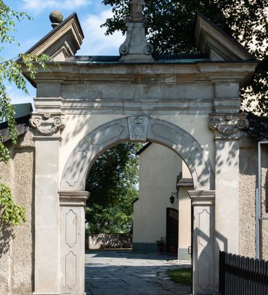 Zdjęcie nr 5: Świątynia otoczona jest murem kamiennym, tynkowanym, nakrytym daszkiem gontowym, jednospadowym. Wejścia znajdują się w murze od strony południowej. Pierwsze, prowadzące do głównych drzwi jest kamienną, późnobarokową bramką z herbem księdza Józefa Sawickiego, datą „1765” oraz figurą św. Jana Kantego. Drugie wejście prowadzi przez dzwonnicę. W murze, od strony wewnętrznej jest 14 wnęk po stacjach drogi krzyżowej. Teren wokół świątyni jest starym cmentarzem, bez zachowanych nagrobków.

Kościół jest budowlą założoną na planie prostokąta, orientowaną, jednonawową z ramionami w rodzaju krótkiego transeptu z wieżą od zachodu, zakrystią i kaplicą od północy oraz kruchtą od południa. Prezbiterium zamknięte jest wielobocznie, trójprzęsłowe, węższe i niższe od nawy. Nawa czteroprzęsłowa, nie jest ulokowana na jednej osi z prezbiterium. 

Artykulacja ścian jest przeprowadzona za pomocą pilastrów toskańskich podtrzymujących sklepienie kolebkowe z lunetami. Ramiona transeptu, kaplica Matki Boskiej Różańcowej oraz kruchta są sklepione krzyżowo. Otwory okienne: w prezbiterium cztery, w nawie cztery od południa, wszystkie zamknięte łukami półkolistymi. Zakrystia piętrowa z jednym oknem na parterze i dwoma na piętrze; od strony północnej kaplica Matki Boskiej Różańcowej z dwoma oknami i jedną, zamurowaną wnęką; obok mała zakrystia. Z prezbiterium do zakrystii prowadzi portal kamienny z inicjałami, herbem i portretem księdza Sawickiego. Na arkadzie tęczowej od strony nawy nowy napis: „FUNDATA A CASIMIRO MAGNO ANNO DOM[INI] 1346”. W pierwszym od strony fasady przęśle znajduje się drewniany chór muzyczny, wsparty na dwóch filarach.

Fasada zachodnia kościoła jest płaska z wieżą, nakryta kopułą z latarnią. Na narożnikach zewnętrznych wieży i naw oraz przy absydzie szkarpy, kryte daszkiem gontowym. Na frontowej ścianie wieży kamienny portal, nad nim sygle „I(osephus) S(awicki) / 1765” oraz herb Nowina. Od strony zachodniej wieża, ozdobiona półkolistymi blendami. Od strony południowej balkonik otoczony żelazną kratą z napisem „1343-1943”. Nad balkonikiem umieszczona jest tarcza zegara, taka sama widnieje od strony północnej, a od zachodniej i wschodniej odpowiadają im tarcze w murze. Przy wieży, od strony północnej wieżyczka w kształcie walca, ścięta od połowy, nakryta daszkiem stożkowym. Przy południowej ścianie wieży między dwiema szkarpami znajduje się kapliczka Ukrzyżowania z figurami Chrystusa Ukrzyżowanego i dwóch łotrów na krzyżach. Dach kościoła siodłowy, kryty gontem.

Na zewnętrznej, południowej ścianie napis: „AEDIFICATA H(A)EC EC[C]LESIA / A[NNO] D[OMINI] / 1606 / PETRVS CZARNY MVLARS”. Niżej wmurowana w półokrągłą wnękę z piaskowca figura Matki Boskiej Niepokalanie Poczętej. Po lewej stronie, u góry fragment fryzu dekoracyjnego, malowany w kolorze czerwonym o motywie zwisających esownic ze stylizowanymi kwiatami i liliami. 

Dzwonnica na planie kwadratu, murowana, otynkowana, dwupiętrowa z sienią przejściową sklepioną, ujętą na zaokrąglonych narożnikach zdwojonymi pilastrami; nakryta gontowym hełmem. Na osi dzwonnicy portal bramy flankowany dwoma pilastrami, o spłaszczonej archiwolcie. Nad belkowaniem monogram maryjny i data „1701”. W sieni na ścianie wschodniej barokowy krucyfiks oraz rzeźby Matki Boskiej i św. Jana Ewangelisty, na ścianie pozostałości polichromii z XVIII wieku.
