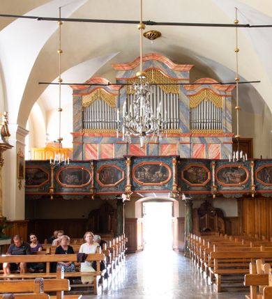 Zdjęcie nr 21: Świątynia otoczona jest murem kamiennym, tynkowanym, nakrytym daszkiem gontowym, jednospadowym. Wejścia znajdują się w murze od strony południowej. Pierwsze, prowadzące do głównych drzwi jest kamienną, późnobarokową bramką z herbem księdza Józefa Sawickiego, datą „1765” oraz figurą św. Jana Kantego. Drugie wejście prowadzi przez dzwonnicę. W murze, od strony wewnętrznej jest 14 wnęk po stacjach drogi krzyżowej. Teren wokół świątyni jest starym cmentarzem, bez zachowanych nagrobków.

Kościół jest budowlą założoną na planie prostokąta, orientowaną, jednonawową z ramionami w rodzaju krótkiego transeptu z wieżą od zachodu, zakrystią i kaplicą od północy oraz kruchtą od południa. Prezbiterium zamknięte jest wielobocznie, trójprzęsłowe, węższe i niższe od nawy. Nawa czteroprzęsłowa, nie jest ulokowana na jednej osi z prezbiterium. 

Artykulacja ścian jest przeprowadzona za pomocą pilastrów toskańskich podtrzymujących sklepienie kolebkowe z lunetami. Ramiona transeptu, kaplica Matki Boskiej Różańcowej oraz kruchta są sklepione krzyżowo. Otwory okienne: w prezbiterium cztery, w nawie cztery od południa, wszystkie zamknięte łukami półkolistymi. Zakrystia piętrowa z jednym oknem na parterze i dwoma na piętrze; od strony północnej kaplica Matki Boskiej Różańcowej z dwoma oknami i jedną, zamurowaną wnęką; obok mała zakrystia. Z prezbiterium do zakrystii prowadzi portal kamienny z inicjałami, herbem i portretem księdza Sawickiego. Na arkadzie tęczowej od strony nawy nowy napis: „FUNDATA A CASIMIRO MAGNO ANNO DOM[INI] 1346”. W pierwszym od strony fasady przęśle znajduje się drewniany chór muzyczny, wsparty na dwóch filarach.

Fasada zachodnia kościoła jest płaska z wieżą, nakryta kopułą z latarnią. Na narożnikach zewnętrznych wieży i naw oraz przy absydzie szkarpy, kryte daszkiem gontowym. Na frontowej ścianie wieży kamienny portal, nad nim sygle „I(osephus) S(awicki) / 1765” oraz herb Nowina. Od strony zachodniej wieża, ozdobiona półkolistymi blendami. Od strony południowej balkonik otoczony żelazną kratą z napisem „1343-1943”. Nad balkonikiem umieszczona jest tarcza zegara, taka sama widnieje od strony północnej, a od zachodniej i wschodniej odpowiadają im tarcze w murze. Przy wieży, od strony północnej wieżyczka w kształcie walca, ścięta od połowy, nakryta daszkiem stożkowym. Przy południowej ścianie wieży między dwiema szkarpami znajduje się kapliczka Ukrzyżowania z figurami Chrystusa Ukrzyżowanego i dwóch łotrów na krzyżach. Dach kościoła siodłowy, kryty gontem.

Na zewnętrznej, południowej ścianie napis: „AEDIFICATA H(A)EC EC[C]LESIA / A[NNO] D[OMINI] / 1606 / PETRVS CZARNY MVLARS”. Niżej wmurowana w półokrągłą wnękę z piaskowca figura Matki Boskiej Niepokalanie Poczętej. Po lewej stronie, u góry fragment fryzu dekoracyjnego, malowany w kolorze czerwonym o motywie zwisających esownic ze stylizowanymi kwiatami i liliami. 

Dzwonnica na planie kwadratu, murowana, otynkowana, dwupiętrowa z sienią przejściową sklepioną, ujętą na zaokrąglonych narożnikach zdwojonymi pilastrami; nakryta gontowym hełmem. Na osi dzwonnicy portal bramy flankowany dwoma pilastrami, o spłaszczonej archiwolcie. Nad belkowaniem monogram maryjny i data „1701”. W sieni na ścianie wschodniej barokowy krucyfiks oraz rzeźby Matki Boskiej i św. Jana Ewangelisty, na ścianie pozostałości polichromii z XVIII wieku.
