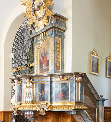Zdjęcie nr 18: Świątynia otoczona jest murem kamiennym, tynkowanym, nakrytym daszkiem gontowym, jednospadowym. Wejścia znajdują się w murze od strony południowej. Pierwsze, prowadzące do głównych drzwi jest kamienną, późnobarokową bramką z herbem księdza Józefa Sawickiego, datą „1765” oraz figurą św. Jana Kantego. Drugie wejście prowadzi przez dzwonnicę. W murze, od strony wewnętrznej jest 14 wnęk po stacjach drogi krzyżowej. Teren wokół świątyni jest starym cmentarzem, bez zachowanych nagrobków.

Kościół jest budowlą założoną na planie prostokąta, orientowaną, jednonawową z ramionami w rodzaju krótkiego transeptu z wieżą od zachodu, zakrystią i kaplicą od północy oraz kruchtą od południa. Prezbiterium zamknięte jest wielobocznie, trójprzęsłowe, węższe i niższe od nawy. Nawa czteroprzęsłowa, nie jest ulokowana na jednej osi z prezbiterium. 

Artykulacja ścian jest przeprowadzona za pomocą pilastrów toskańskich podtrzymujących sklepienie kolebkowe z lunetami. Ramiona transeptu, kaplica Matki Boskiej Różańcowej oraz kruchta są sklepione krzyżowo. Otwory okienne: w prezbiterium cztery, w nawie cztery od południa, wszystkie zamknięte łukami półkolistymi. Zakrystia piętrowa z jednym oknem na parterze i dwoma na piętrze; od strony północnej kaplica Matki Boskiej Różańcowej z dwoma oknami i jedną, zamurowaną wnęką; obok mała zakrystia. Z prezbiterium do zakrystii prowadzi portal kamienny z inicjałami, herbem i portretem księdza Sawickiego. Na arkadzie tęczowej od strony nawy nowy napis: „FUNDATA A CASIMIRO MAGNO ANNO DOM[INI] 1346”. W pierwszym od strony fasady przęśle znajduje się drewniany chór muzyczny, wsparty na dwóch filarach.

Fasada zachodnia kościoła jest płaska z wieżą, nakryta kopułą z latarnią. Na narożnikach zewnętrznych wieży i naw oraz przy absydzie szkarpy, kryte daszkiem gontowym. Na frontowej ścianie wieży kamienny portal, nad nim sygle „I(osephus) S(awicki) / 1765” oraz herb Nowina. Od strony zachodniej wieża, ozdobiona półkolistymi blendami. Od strony południowej balkonik otoczony żelazną kratą z napisem „1343-1943”. Nad balkonikiem umieszczona jest tarcza zegara, taka sama widnieje od strony północnej, a od zachodniej i wschodniej odpowiadają im tarcze w murze. Przy wieży, od strony północnej wieżyczka w kształcie walca, ścięta od połowy, nakryta daszkiem stożkowym. Przy południowej ścianie wieży między dwiema szkarpami znajduje się kapliczka Ukrzyżowania z figurami Chrystusa Ukrzyżowanego i dwóch łotrów na krzyżach. Dach kościoła siodłowy, kryty gontem.

Na zewnętrznej, południowej ścianie napis: „AEDIFICATA H(A)EC EC[C]LESIA / A[NNO] D[OMINI] / 1606 / PETRVS CZARNY MVLARS”. Niżej wmurowana w półokrągłą wnękę z piaskowca figura Matki Boskiej Niepokalanie Poczętej. Po lewej stronie, u góry fragment fryzu dekoracyjnego, malowany w kolorze czerwonym o motywie zwisających esownic ze stylizowanymi kwiatami i liliami. 

Dzwonnica na planie kwadratu, murowana, otynkowana, dwupiętrowa z sienią przejściową sklepioną, ujętą na zaokrąglonych narożnikach zdwojonymi pilastrami; nakryta gontowym hełmem. Na osi dzwonnicy portal bramy flankowany dwoma pilastrami, o spłaszczonej archiwolcie. Nad belkowaniem monogram maryjny i data „1701”. W sieni na ścianie wschodniej barokowy krucyfiks oraz rzeźby Matki Boskiej i św. Jana Ewangelisty, na ścianie pozostałości polichromii z XVIII wieku.
