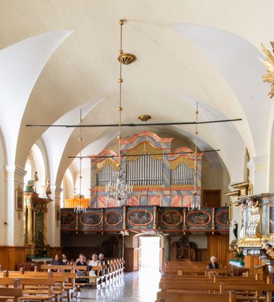 Zdjęcie nr 20: Świątynia otoczona jest murem kamiennym, tynkowanym, nakrytym daszkiem gontowym, jednospadowym. Wejścia znajdują się w murze od strony południowej. Pierwsze, prowadzące do głównych drzwi jest kamienną, późnobarokową bramką z herbem księdza Józefa Sawickiego, datą „1765” oraz figurą św. Jana Kantego. Drugie wejście prowadzi przez dzwonnicę. W murze, od strony wewnętrznej jest 14 wnęk po stacjach drogi krzyżowej. Teren wokół świątyni jest starym cmentarzem, bez zachowanych nagrobków.

Kościół jest budowlą założoną na planie prostokąta, orientowaną, jednonawową z ramionami w rodzaju krótkiego transeptu z wieżą od zachodu, zakrystią i kaplicą od północy oraz kruchtą od południa. Prezbiterium zamknięte jest wielobocznie, trójprzęsłowe, węższe i niższe od nawy. Nawa czteroprzęsłowa, nie jest ulokowana na jednej osi z prezbiterium. 

Artykulacja ścian jest przeprowadzona za pomocą pilastrów toskańskich podtrzymujących sklepienie kolebkowe z lunetami. Ramiona transeptu, kaplica Matki Boskiej Różańcowej oraz kruchta są sklepione krzyżowo. Otwory okienne: w prezbiterium cztery, w nawie cztery od południa, wszystkie zamknięte łukami półkolistymi. Zakrystia piętrowa z jednym oknem na parterze i dwoma na piętrze; od strony północnej kaplica Matki Boskiej Różańcowej z dwoma oknami i jedną, zamurowaną wnęką; obok mała zakrystia. Z prezbiterium do zakrystii prowadzi portal kamienny z inicjałami, herbem i portretem księdza Sawickiego. Na arkadzie tęczowej od strony nawy nowy napis: „FUNDATA A CASIMIRO MAGNO ANNO DOM[INI] 1346”. W pierwszym od strony fasady przęśle znajduje się drewniany chór muzyczny, wsparty na dwóch filarach.

Fasada zachodnia kościoła jest płaska z wieżą, nakryta kopułą z latarnią. Na narożnikach zewnętrznych wieży i naw oraz przy absydzie szkarpy, kryte daszkiem gontowym. Na frontowej ścianie wieży kamienny portal, nad nim sygle „I(osephus) S(awicki) / 1765” oraz herb Nowina. Od strony zachodniej wieża, ozdobiona półkolistymi blendami. Od strony południowej balkonik otoczony żelazną kratą z napisem „1343-1943”. Nad balkonikiem umieszczona jest tarcza zegara, taka sama widnieje od strony północnej, a od zachodniej i wschodniej odpowiadają im tarcze w murze. Przy wieży, od strony północnej wieżyczka w kształcie walca, ścięta od połowy, nakryta daszkiem stożkowym. Przy południowej ścianie wieży między dwiema szkarpami znajduje się kapliczka Ukrzyżowania z figurami Chrystusa Ukrzyżowanego i dwóch łotrów na krzyżach. Dach kościoła siodłowy, kryty gontem.

Na zewnętrznej, południowej ścianie napis: „AEDIFICATA H(A)EC EC[C]LESIA / A[NNO] D[OMINI] / 1606 / PETRVS CZARNY MVLARS”. Niżej wmurowana w półokrągłą wnękę z piaskowca figura Matki Boskiej Niepokalanie Poczętej. Po lewej stronie, u góry fragment fryzu dekoracyjnego, malowany w kolorze czerwonym o motywie zwisających esownic ze stylizowanymi kwiatami i liliami. 

Dzwonnica na planie kwadratu, murowana, otynkowana, dwupiętrowa z sienią przejściową sklepioną, ujętą na zaokrąglonych narożnikach zdwojonymi pilastrami; nakryta gontowym hełmem. Na osi dzwonnicy portal bramy flankowany dwoma pilastrami, o spłaszczonej archiwolcie. Nad belkowaniem monogram maryjny i data „1701”. W sieni na ścianie wschodniej barokowy krucyfiks oraz rzeźby Matki Boskiej i św. Jana Ewangelisty, na ścianie pozostałości polichromii z XVIII wieku.
