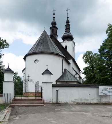 Zdjęcie nr 19: Kościół św. Piotra i św. Pawła jest usytuowany w centrum Łapsz Wyżnych, na południe od głównej drogi z Trybsza do Łapsz Niżnych. Teren przykościelny jest otoczony wysokim kamiennym i częściowo otynkowanym murem, nakrytym gontem od strony wschodniej, zachodniej i północnej oraz nakrytym blachą od strony południowej; daszki jednospadowe, nachylone na zewnątrz. W części zachodniej muru zlokalizowana jest szeroka brama, flankowana dwoma masywnymi filarami, na których ustawione są okrągłe słupy, przykryte stożkowym daszkiem gontowym i zwieńczone krzyżykami. Od wschodu analogiczne wejście z szerszym przejściem, dostępnym schodkami. Trzecie wejście na teren przykościelny prowadzi od północy przez bramę w kształcie arkady zamkniętej łukiem odcinkowym, zwieńczonej trójkątnym nadprożem, na którego szczycie ustawiony jest krzyż i wazony po bokach. Czwarte wejście zlokalizowane w zachodnio-południowym narożniku muru prowadzi przez wysokie schody z balustradą. Od zachodu w ogrodzeniu ulokowany jest budynek salki katechetycznej (dawna kostnica) wchodzącej w mur ścianą frontową. W obrębie placu przykościelnego znajdują się resztki cmentarza w postaci kamiennych i granitowych nagrobków oraz żeliwnych krzyży. 

Kościół jest orientowany, murowany, otynkowany, jednonawowy z czworoboczną wieżą w fasadzie z prezbiterium zamkniętym półkoliście. Dwuprzęsłowe prezbiterium oddziela od nawy ściana arkady tęczowej. Nawa jest szersza, trójprzęsłowa. Wnętrze artykułowane pilastrami wspierającymi sklepienie kolebkowe z lunetami na gurtach, ozdobione stiukowymi, późnobarokowymi ramami. Od południa do prezbiterium przylega zakrystia na planie prostokąta, a do nawy od północny kruchta z portalem z zaakcentowaną datą: „1760”. Na zachodniej ścianie nawy chór muzyczny wsparty jest na trzech półkolistych arkadach. 

Wnętrze oświetlają umieszczone w południowych i północnych ścianach nawy prostokątne, zamknięte półkoliście cztery okna, takie same dwa znajdują się w prezbiterium; w wieży trzy podobne okna umieszczone po jednym z każdej strony, oprócz ściany zachodniej; w apsydzie jedno małe, okrągłe okno. Do kościoła prowadzi główne wejście od strony zachodniej oraz dwa mniejsze od strony północnej przez kruchtę i od strony południowej przez zakrystię.

W zewnętrznej elewacji kościoła widoczny jest niewysoki, kamienny cokół, powyżej kościół jest otynkowany. Prezbiterium, niższe od nawy. Nawa oszkarpowana, nakryta dachem dwuspadowym z wieżą na sygnaturkę na skrzyżowaniu na wschodnim zakończeniu nawy. Do zachodniej fasady kościoła dostawiona jest wysoka założona na planie kwadratu wieża-dzwonnica. W dolnej kondygnacji na osi kościoła znajduje się prostokątne wejście do kruchty, zamknięte półkoliście. Fasada wieży w całości pokryta jest blachą, przechodzącą nad głównym wejściem do kościoła w daszek. Hełm wieży baniasty z latarnią.
