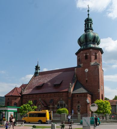 Zdjęcie nr 2: Kościół św. Jana Chrzciciela w Zembrzycach jest usytuowany na zachód od głównej drogi prowadzącej z Makowa Podhalańskiego do Wadowic i położony w centrum wsi, na placu otoczonym żeliwnym płotem na kamiennej podmurówce. Wejście na plac przykościelny prowadzi przez bramę od zachodu i wąską bramkę od północy. Kościół jest budowlą orientowaną, założoną na planie prostokąta, trójnawową, pseudohalową z prezbiterium zamkniętym trójbocznie, przy którym od północy znajduje się kaplica, a od południa piętrowa zakrystia z przedsionkiem i emporą otwartą na prezbiterium. Do nawy od strony północnej przylega wąska kruchta, nakryta dwuspadowym daszkiem. Od zachodu świątyni jest czworoboczna, masywna wieża, w górnej jednej trzeciej wysokości ośmioboczna, nakryta hełmem baniastym z latarnią. W fasadzie wysoka, półkolista wnęka z portalem i oknem termalnym. Przy wieży od północny składzik, a od południa kaplica. Ściany prezbiterium, nawy oraz elewacje aneksów w narożnikach artykułowane są szkarpami. Elewacje boczne zwieńczone ceglanym, zygzakowatym fryzem z krzyżykami. Szczyty na zakończeniach korpusu ozdobione kamiennymi szyszkami. W nawie okna trójdzielne z kamiennymi przezroczami, zamknięte łukami półkolistymi; w prezbiterium prostokątne zamknięte półkoliście. Świątynia nakryta jest dachem dwuspadowym. Na zakończeniu nawy znajduje się wieżyczka na sygnaturkę z baniastym hełmem. Wewnątrz nawy oddzielone są kolumnami z ośmiobocznymi głowicami, które wspierają sklepienia kolebkowe z lunetami. Empory i kaplice otwarte są arkadami półkolistymi. Prezbiterium podniesione jest o poziom dwóch stopni.
