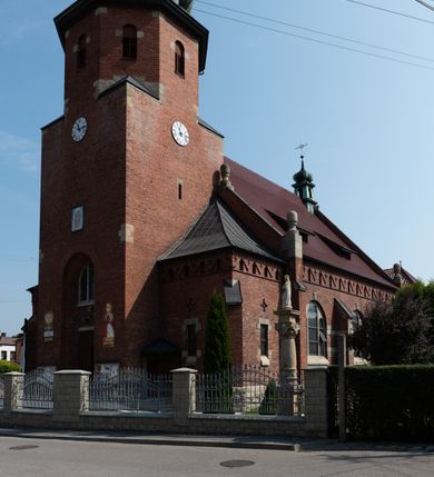 Zdjęcie nr 10: Kościół św. Jana Chrzciciela w Zembrzycach jest usytuowany na zachód od głównej drogi prowadzącej z Makowa Podhalańskiego do Wadowic i położony w centrum wsi, na placu otoczonym żeliwnym płotem na kamiennej podmurówce. Wejście na plac przykościelny prowadzi przez bramę od zachodu i wąską bramkę od północy. Kościół jest budowlą orientowaną, założoną na planie prostokąta, trójnawową, pseudohalową z prezbiterium zamkniętym trójbocznie, przy którym od północy znajduje się kaplica, a od południa piętrowa zakrystia z przedsionkiem i emporą otwartą na prezbiterium. Do nawy od strony północnej przylega wąska kruchta, nakryta dwuspadowym daszkiem. Od zachodu świątyni jest czworoboczna, masywna wieża, w górnej jednej trzeciej wysokości ośmioboczna, nakryta hełmem baniastym z latarnią. W fasadzie wysoka, półkolista wnęka z portalem i oknem termalnym. Przy wieży od północny składzik, a od południa kaplica. Ściany prezbiterium, nawy oraz elewacje aneksów w narożnikach artykułowane są szkarpami. Elewacje boczne zwieńczone ceglanym, zygzakowatym fryzem z krzyżykami. Szczyty na zakończeniach korpusu ozdobione kamiennymi szyszkami. W nawie okna trójdzielne z kamiennymi przezroczami, zamknięte łukami półkolistymi; w prezbiterium prostokątne zamknięte półkoliście. Świątynia nakryta jest dachem dwuspadowym. Na zakończeniu nawy znajduje się wieżyczka na sygnaturkę z baniastym hełmem. Wewnątrz nawy oddzielone są kolumnami z ośmiobocznymi głowicami, które wspierają sklepienia kolebkowe z lunetami. Empory i kaplice otwarte są arkadami półkolistymi. Prezbiterium podniesione jest o poziom dwóch stopni.
