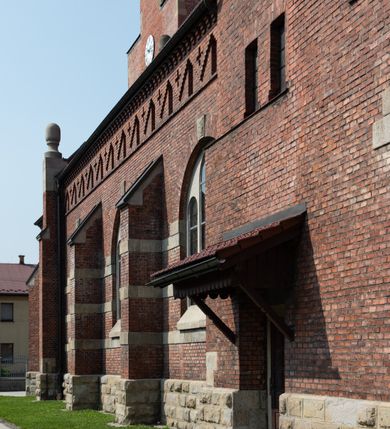 Zdjęcie nr 25: Kościół św. Jana Chrzciciela w Zembrzycach jest usytuowany na zachód od głównej drogi prowadzącej z Makowa Podhalańskiego do Wadowic i położony w centrum wsi, na placu otoczonym żeliwnym płotem na kamiennej podmurówce. Wejście na plac przykościelny prowadzi przez bramę od zachodu i wąską bramkę od północy. Kościół jest budowlą orientowaną, założoną na planie prostokąta, trójnawową, pseudohalową z prezbiterium zamkniętym trójbocznie, przy którym od północy znajduje się kaplica, a od południa piętrowa zakrystia z przedsionkiem i emporą otwartą na prezbiterium. Do nawy od strony północnej przylega wąska kruchta, nakryta dwuspadowym daszkiem. Od zachodu świątyni jest czworoboczna, masywna wieża, w górnej jednej trzeciej wysokości ośmioboczna, nakryta hełmem baniastym z latarnią. W fasadzie wysoka, półkolista wnęka z portalem i oknem termalnym. Przy wieży od północny składzik, a od południa kaplica. Ściany prezbiterium, nawy oraz elewacje aneksów w narożnikach artykułowane są szkarpami. Elewacje boczne zwieńczone ceglanym, zygzakowatym fryzem z krzyżykami. Szczyty na zakończeniach korpusu ozdobione kamiennymi szyszkami. W nawie okna trójdzielne z kamiennymi przezroczami, zamknięte łukami półkolistymi; w prezbiterium prostokątne zamknięte półkoliście. Świątynia nakryta jest dachem dwuspadowym. Na zakończeniu nawy znajduje się wieżyczka na sygnaturkę z baniastym hełmem. Wewnątrz nawy oddzielone są kolumnami z ośmiobocznymi głowicami, które wspierają sklepienia kolebkowe z lunetami. Empory i kaplice otwarte są arkadami półkolistymi. Prezbiterium podniesione jest o poziom dwóch stopni.

