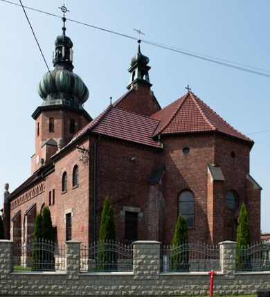 Zdjęcie nr 29: Kościół św. Jana Chrzciciela w Zembrzycach jest usytuowany na zachód od głównej drogi prowadzącej z Makowa Podhalańskiego do Wadowic i położony w centrum wsi, na placu otoczonym żeliwnym płotem na kamiennej podmurówce. Wejście na plac przykościelny prowadzi przez bramę od zachodu i wąską bramkę od północy. Kościół jest budowlą orientowaną, założoną na planie prostokąta, trójnawową, pseudohalową z prezbiterium zamkniętym trójbocznie, przy którym od północy znajduje się kaplica, a od południa piętrowa zakrystia z przedsionkiem i emporą otwartą na prezbiterium. Do nawy od strony północnej przylega wąska kruchta, nakryta dwuspadowym daszkiem. Od zachodu świątyni jest czworoboczna, masywna wieża, w górnej jednej trzeciej wysokości ośmioboczna, nakryta hełmem baniastym z latarnią. W fasadzie wysoka, półkolista wnęka z portalem i oknem termalnym. Przy wieży od północny składzik, a od południa kaplica. Ściany prezbiterium, nawy oraz elewacje aneksów w narożnikach artykułowane są szkarpami. Elewacje boczne zwieńczone ceglanym, zygzakowatym fryzem z krzyżykami. Szczyty na zakończeniach korpusu ozdobione kamiennymi szyszkami. W nawie okna trójdzielne z kamiennymi przezroczami, zamknięte łukami półkolistymi; w prezbiterium prostokątne zamknięte półkoliście. Świątynia nakryta jest dachem dwuspadowym. Na zakończeniu nawy znajduje się wieżyczka na sygnaturkę z baniastym hełmem. Wewnątrz nawy oddzielone są kolumnami z ośmiobocznymi głowicami, które wspierają sklepienia kolebkowe z lunetami. Empory i kaplice otwarte są arkadami półkolistymi. Prezbiterium podniesione jest o poziom dwóch stopni.
