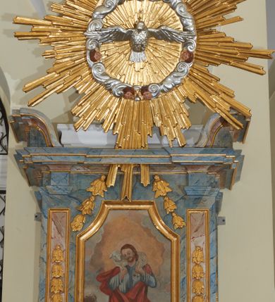 Zdjęcie nr 7: Ambona przyścienna, wisząca, z jednobiegowymi schodami dostępnymi od prawej strony. Kosz na planie kwadratu o ściętych narożach i wklęsło-wypukłym profilu. U spodu ośmioboczne podwieszenie zwężające się ku dołowi, ujęte parą spływów wolutowych utworzonych z liści akantu, u dołu zakończone szyszką. Cokół kosza zdobiony puklowaniem, dekorowany trzema kartuszami utworzonymi z karbowanej wstęgi, zwieńczonymi płaskimi, symetrycznymi palmetami, z główkami aniołków skierowanymi na wprost i umieszczonymi u dołu. Naroża kosza ozdobione spływami wolutowymi o karbowanych trzonach, ozdobionych kampanulami, podtrzymującymi belkowanie, stanowiące parapet z silnie wysuniętym gzymsem. Na fryzie parapetu uskrzydlone główki anielskie.

Ściany dekorowane są płycinami w formie stojących prostokątów, naprzemiennie wybrzuszonych lub wklęsłych z przedstawieniami czterech ewangelistów, ujętymi w złocone ramy. Od lewej: św. Mateusz, św. Marek, św. Łukasz i św. Jan. Święty Mateusz siedzi zwrócony trzy czwarte w lewo i pisze piórem w księdze. Obok stoi uskrzydlony człowiek, który obejmuje go za szyję, ubrany w niebieską suknię odsłaniającą klatkę piersiową i złoty płaszcz z końcem rozwianym ku górze. Święty ma rysy twarzy starszego człowieka z długą i siwą brodą oraz siwymi włosami. Ubrany jest w obszerny czerwony płaszcz i sandały. Scena ukazana jest we wnętrzu architektonicznym. Święty Marek również został ukazany w swojej pracowni. Siedzi, zwrócony trzy czwarte w lewo przy stoliku i pisząc w księdze, odwraca się w prawo, gdzie spoczywa lew – jego atrybut. Ma siwą brodę. Ubrany jest w niebieską suknię, zapinaną z przodu na guziki oraz czerwony płaszcz przewieszony przez prawe ramię. Stolik zasłany jest jasnozielonym obrusem, na którym leży otwarta księga i czerwony kałamarz. Na ścianie, ponad stolikiem wisi półka z książkami. Po lewej stronie obrazu widać otwartą przestrzeń z widokiem na góry, w pozostałej brązowe ściany pokoju, w którym znajduje się święty. Na kolejnym obrazie św. Łukasz siedzi zwrócony trzy czwarte w prawo, przy stoliku z pulpitem i o wolutowych nóżkach. W prawej dłoni trzyma pióro, którym pisze na karcie papieru. Ubrany jest z jasnobrązową suknię, niebieski płaszcz owijający nogi i niebieskie sandały; na głowie ma założoną czapkę. Po prawej stronie obrazu stoi jego atrybut – wół. Całość ukazana jest we wnętrzu architektonicznym z półkolistą arkadą po prawej stronie. Święty Jan został ukazany na tle krajobrazu, zwrócony jest trzy czwarte w prawo, pisze na karcie papieru. Ubrany jest w jasnozieloną suknię i czerwony płaszcz. Ma długie włosy, spływające na plecy, został ukazany bez zarostu. Po prawej stronie wysokie drzewo, w oddali pejzaż górski. Wszyscy ewangeliści mają okrągłe nimby z wpisaną w polu gwiazdą. 

Zaplecek w formie stojącego prostopadłościanu z niepełnym belkowaniem, wspartym na podwieszonych impostach, podtrzymującym odwrócony, przerywany przyczółek. Na ściance frontowej płycina w kształcie stojącego prostokąta o wklęsłych górnych narożach z obrazem Dobrego Pasterza w polu. Po bokach flankowana dwiema wąskimi płycinami, zdobionymi zwisem z kampanul. Na ściankach bocznych analogiczne płyciny z kampanulami. Chrystus ukazany frontalnie z barankiem na barkach, którego przytrzymuje rękami za nóżki. Zbawiciel ma owalną twarz z krótkim zarostem i jasnobrązowymi włosami, spływającymi na lewe ramię. Ubrany jest w biało-niebieską suknię oraz czerwony płaszcz. W oddali pejzaż z miastem po lewej, u góry szaro-złote niebo. Po lewej u dołu sygnatura „A D L”. Całość zwieńczona promienistą glorią z gołębicą Ducha Świętego w otoku utworzonym z chmur i główek anielskich. Struktura marmoryzowana w kolorze niebieskim, a płyciny w kolorze jasnoróżowym; ornamentyka, gloria i profile złocone i srebrzone.
