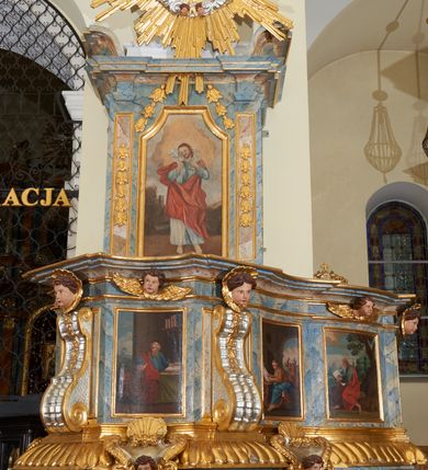Zdjęcie nr 2: Ambona przyścienna, wisząca, z jednobiegowymi schodami dostępnymi od prawej strony. Kosz na planie kwadratu o ściętych narożach i wklęsło-wypukłym profilu. U spodu ośmioboczne podwieszenie zwężające się ku dołowi, ujęte parą spływów wolutowych utworzonych z liści akantu, u dołu zakończone szyszką. Cokół kosza zdobiony puklowaniem, dekorowany trzema kartuszami utworzonymi z karbowanej wstęgi, zwieńczonymi płaskimi, symetrycznymi palmetami, z główkami aniołków skierowanymi na wprost i umieszczonymi u dołu. Naroża kosza ozdobione spływami wolutowymi o karbowanych trzonach, ozdobionych kampanulami, podtrzymującymi belkowanie, stanowiące parapet z silnie wysuniętym gzymsem. Na fryzie parapetu uskrzydlone główki anielskie.

Ściany dekorowane są płycinami w formie stojących prostokątów, naprzemiennie wybrzuszonych lub wklęsłych z przedstawieniami czterech ewangelistów, ujętymi w złocone ramy. Od lewej: św. Mateusz, św. Marek, św. Łukasz i św. Jan. Święty Mateusz siedzi zwrócony trzy czwarte w lewo i pisze piórem w księdze. Obok stoi uskrzydlony człowiek, który obejmuje go za szyję, ubrany w niebieską suknię odsłaniającą klatkę piersiową i złoty płaszcz z końcem rozwianym ku górze. Święty ma rysy twarzy starszego człowieka z długą i siwą brodą oraz siwymi włosami. Ubrany jest w obszerny czerwony płaszcz i sandały. Scena ukazana jest we wnętrzu architektonicznym. Święty Marek również został ukazany w swojej pracowni. Siedzi, zwrócony trzy czwarte w lewo przy stoliku i pisząc w księdze, odwraca się w prawo, gdzie spoczywa lew – jego atrybut. Ma siwą brodę. Ubrany jest w niebieską suknię, zapinaną z przodu na guziki oraz czerwony płaszcz przewieszony przez prawe ramię. Stolik zasłany jest jasnozielonym obrusem, na którym leży otwarta księga i czerwony kałamarz. Na ścianie, ponad stolikiem wisi półka z książkami. Po lewej stronie obrazu widać otwartą przestrzeń z widokiem na góry, w pozostałej brązowe ściany pokoju, w którym znajduje się święty. Na kolejnym obrazie św. Łukasz siedzi zwrócony trzy czwarte w prawo, przy stoliku z pulpitem i o wolutowych nóżkach. W prawej dłoni trzyma pióro, którym pisze na karcie papieru. Ubrany jest z jasnobrązową suknię, niebieski płaszcz owijający nogi i niebieskie sandały; na głowie ma założoną czapkę. Po prawej stronie obrazu stoi jego atrybut – wół. Całość ukazana jest we wnętrzu architektonicznym z półkolistą arkadą po prawej stronie. Święty Jan został ukazany na tle krajobrazu, zwrócony jest trzy czwarte w prawo, pisze na karcie papieru. Ubrany jest w jasnozieloną suknię i czerwony płaszcz. Ma długie włosy, spływające na plecy, został ukazany bez zarostu. Po prawej stronie wysokie drzewo, w oddali pejzaż górski. Wszyscy ewangeliści mają okrągłe nimby z wpisaną w polu gwiazdą. 

Zaplecek w formie stojącego prostopadłościanu z niepełnym belkowaniem, wspartym na podwieszonych impostach, podtrzymującym odwrócony, przerywany przyczółek. Na ściance frontowej płycina w kształcie stojącego prostokąta o wklęsłych górnych narożach z obrazem Dobrego Pasterza w polu. Po bokach flankowana dwiema wąskimi płycinami, zdobionymi zwisem z kampanul. Na ściankach bocznych analogiczne płyciny z kampanulami. Chrystus ukazany frontalnie z barankiem na barkach, którego przytrzymuje rękami za nóżki. Zbawiciel ma owalną twarz z krótkim zarostem i jasnobrązowymi włosami, spływającymi na lewe ramię. Ubrany jest w biało-niebieską suknię oraz czerwony płaszcz. W oddali pejzaż z miastem po lewej, u góry szaro-złote niebo. Po lewej u dołu sygnatura „A D L”. Całość zwieńczona promienistą glorią z gołębicą Ducha Świętego w otoku utworzonym z chmur i główek anielskich. Struktura marmoryzowana w kolorze niebieskim, a płyciny w kolorze jasnoróżowym; ornamentyka, gloria i profile złocone i srebrzone.
