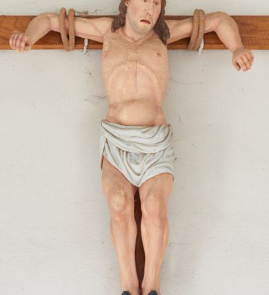 Zdjęcie nr 1: Dobry Łotr zawieszony na krzyżu na wyciągniętych ramionach, przywiązanych podwójnym sznurem z przedramionami opuszczonymi w dół, stopy przebite dwoma gwoździami, kolana ugięte, głowa przechylona na lewe ramię. Klatka piersiowa szeroka o wyraźnie podkreślonej linii żeber i mostka z głęboko zaznaczonym wcięciem w talii. Twarz podłużna z długim nosem i migdałowymi oczami, okolonymi regularnymi łukami brwiowymi, usta rozchylone z opuszczonymi kącikami, widoczny delikatny zarost. Włosy długie, ciemnobrązowe, opadające na ramiona i plecy. Święty ma zawiązaną wokół bioder białą przepaskę, ciasno zawiązaną. Z ran na stopach spływają strużki krwi. Krzyż gładki, drewniany. Polichromia rzeźby naturalistyczna. 