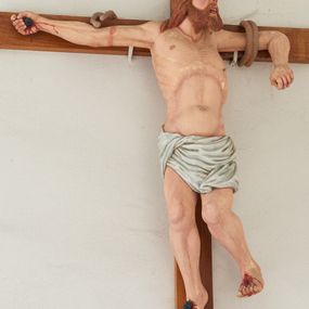 Zdjęcie nr 1: Rzeźba Złego Łotra na krzyżu ukazana w ekspresyjnej pozie o esowato wygiętej sylwetce z głową zwróconą w lewo. Ramiona ułożone wzdłuż patibulum, przywiązane do niego podwójnym sznurem (na prawej ręce urwanym). Prawa ręka wyprostowana i przybita gwoździem do krzyża, a lewa zgięta w łokciu z przedramieniem zwróconym w dół; dłonie zaciśnięte. Klatka piersiowa szeroka o wyraźnie podkreślonej linii żeber i mostka z głęboko zaznaczonym wcięciem w talii. Prawa noga przybita do krzyża jednym gwoździem, lewa ugięta w kolanie i uniesiona bok z raną po gwoździu w stopie. Twarz podłużna, okolona brodą; usta otwarte i ukazujące rzędy białych zębów; duże, szeroko otwarte oczy; szeroki nos; długie i jasnobrązowe włosy. Łotr przewiązany jest w biodrach białą, drapowaną, ciasno opinającą biodra przepaską. Na stopach i prawej dłoni widoczne są ślady krwi. Polichromia rzeźby jest naturalistyczna; krzyż drewniany, gładki.