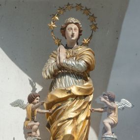Zdjęcie nr 1: Figura Matki Boskiej Niepokalanie Poczętej umieszczona we wnęce na sześciobocznym cokole. Maria ukazana frontalnie, stojąca na zielonym półksiężycu, w kontrapoście, z prawą nogą ugiętą w kolanie, z rękami złożonymi w geście modlitwy. Twarz podłużna z małymi ustami, długim nosem i oczami skierowanymi na wprost, okolona bujnymi włosami, spiętymi z tyłu. Ubrana jest w ciasno przylegającą do ciała srebrzoną suknię, przewiązaną w talii, złocony płaszcz zasłaniający dekolt, lewe ramię i nogi. Na głowie ma założoną małą chustkę, a wokół niej duży nimb złożony z 12 gwiazd zawieszonych na metalowym pręcie. U dołu znajdują się dwie uskrzydlone główki aniołków w ekspresyjnych pozach. Całość flankują dwa pionowe spływy wolutowe utworzone z liści akantu, na których szczycie, na małych obłokach stoją dwa aniołki, zwrócone ku Matce Bożej. Aniołki przyklękają na jednym kolanie, ręce wyciągają przed siebie, mają szeroko rozłożone skrzydła. Twarze o rysach dziecięcych, okryte bujnymi, ciemnymi, średniej długości włosami, zasłaniającymi uszy. Ubrane są w złote przepaski, przerzucone jednym końcem przez ramię. Polichromia w odsłoniętych partiach ciała naturalistyczna, szaty i detale złocone i srebrzone, półksiężyc w kolorze zielonym, pokryty laserunkiem. Pod niszą z figurą znajduje się płaskorzeźbiony monogram maryjny z napisem „A(NNO) D(OMINI) 1701”.