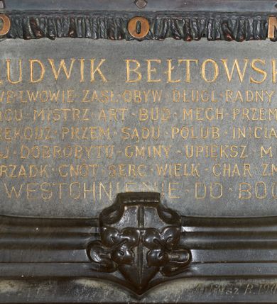 Zdjęcie nr 6: Epitafium w kształcie stojącego prostokąta, dwustopniowe, oddzielone wąskim gzymsem, zamknięte łukiem półkolistym, na którego zakończeniach dwie puste tarcze herbowe. W dolnej części epitafium płycina w kształcie leżącego prostokąta o fantazyjnym wykroju, w narożach ujęta dwiema czołgankami, z inskrypcją w polu: „LUDWIK BEŁTOWSKI / UR[ODZONY] 1819 WE LWOWIE ZASŁ[UŻONY] OBYW[ATEL] DŁUG[O]L[ETNI] RADNY MIASTA / NOWEGO TARGU MISTRZ ART[YSTA] BUD[OWLI] MECH[ANICZNYCH] PRZEM[YSŁOWYCH] PRZEWODN[ICZĄCY] / POW[IATOWEGO] STOW[ARZYSZENIA] RĘKODZ[IĘLNIKÓW] PRZEM[YSŁOWYCH] SĄDU POLUB[OWNEGO] INICIAT[OR] CZYNN[Y] ORĘD[OWNIK] / POWIĘKSZ[ANIA] MAJ[ĄTKU] DOBROBYTU GMINY UPIĘKSZ[ANIA] MIASTA OFIARN[Y] / PATRIOT[A] MĄŻ RZADK[ICH] CNÓT SERC[A] WIELK[IEGO] CHAR[AKTERU] ZM[ARŁ] 13. STYCZ[NIA] 1902 / PROSI O WESTCHNIENIE DO BOGA AMEN”. W prawym dolnym rogu epitafium sygnatura „Juliusz B[ełtowski] 1904.” Powyżej kwadratowy odlew z przedstawieniem Miłosiernego Samarytanina, flankowany dwiema popiersiami: rzeźbą Matki Boskiej z Dzieciątkiem po prawej i św. Józefa Robotnika po lewej. W dolnej części odlewu litery „D[EO] O[PTIMO] M[AXIMO]”. Na odlewie ukazany leżący na ziemi mężczyzna o wychudzonej posturze, któremu Samarytanin podaje kubek z wodą do picia. Po lewej stronie obrazu głowa wielbłąda. Matka Boska zwrócona trzy czwarte w lewo, z głową pochyloną w dół, przytulająca do piersi śpiące Dzieciątko. W dłoniach trzyma księgę. Twarz o wyraźnych rysach z długim nosem i zaciśniętymi ustami. Ubrana jest w suknię z długimi rękawami i płaszcz założony na głowę. Święty Józef zwrócony jest delikatnie w prawo z głową skierowaną w lewo. Ma krótkie i bujne włosy, wzrok skierowany w prawo oraz zaciśnięte usta. Ubrany jest w strój robotnika – koszulę z podwiniętymi do łokci rękawami. W dłoniach trzyma strug i piłę do drewna. W górnej części epitafium znajduje się okrągłe popiersie Ludwika Bełtowskiego w szerokiej okrągłej ramie. Zmarły ukazany z prawego profilu o podłużnej twarzy ze spiczastą brodą i wąsami, długim nosem i zmarszczonym czołem. Włosy krótkie. Ubrany jest w koszulę i marynarkę. Po lewej stronie popiersia sygnatura „B[ełtowski] [1]902”.



