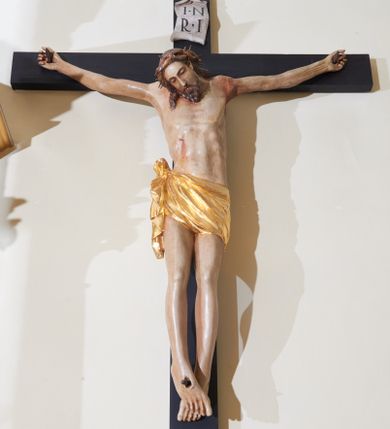 Zdjęcie nr 1: Rzeźba Chrystusa przybita do krzyża trzema gwoździami, ukazana w typie Cristo morte. Ciało w delikatnym zwisie, sylwetka wydłużona o delikatnie podkreślonej anatomii, nogi lekko ugięte w kolanach. Chrystus ma głowę przechyloną na prawe ramię. Twarz szczupła, z wąskim i długim nosem, zamkniętymi oczami, okolona krótką brodą. Włosy długie ze skręconym lokiem spływającym do przodu po prawej stronie, na głowie założona korona cierniowa. Perizonium zawiązane na węzeł na prawym boku, z jednym końcem zwisającym wzdłuż prawej nogi, złocone. Polichromia ciała naturalistyczna. Krzyż gładki, nad głową Chrystusa titulus w formie pionowej banderoli z napisem „IN / RI”. 
