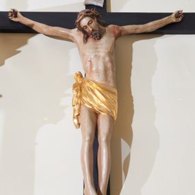 Zdjęcie nr 1: Rzeźba Chrystusa przybita do krzyża trzema gwoździami, ukazana w typie Cristo morte. Ciało w delikatnym zwisie, sylwetka wydłużona o delikatnie podkreślonej anatomii, nogi lekko ugięte w kolanach. Chrystus ma głowę przechyloną na prawe ramię. Twarz szczupła, z wąskim i długim nosem, zamkniętymi oczami, okolona krótką brodą. Włosy długie ze skręconym lokiem spływającym do przodu po prawej stronie, na głowie założona korona cierniowa. Perizonium zawiązane na węzeł na prawym boku, z jednym końcem zwisającym wzdłuż prawej nogi, złocone. Polichromia ciała naturalistyczna. Krzyż gładki, nad głową Chrystusa titulus w formie pionowej banderoli z napisem „IN / RI”. 
