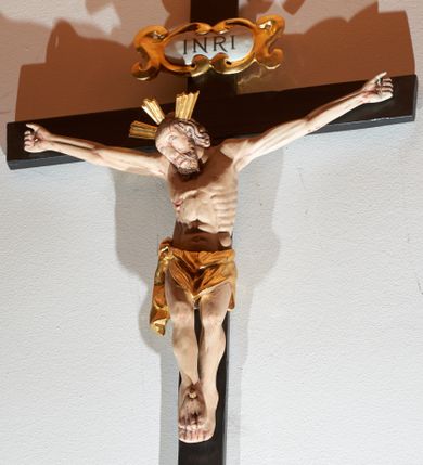 Zdjęcie nr 1: Krucyfiks z rzeźbą Chrystusa w typie Cristo morte. Rzeźba pełna; głowa przechylona na prawe ramię; nogi delikatnie ugięte w kolanach, stopy przebite jednym gwoździem w układzie prawa na lewą. Twarz pociągła, o wyraźnych rysach, okolona jasnobrązową brodą. Na głowie Chrystus ma nimb krzyżowy złożony z trzech wiązek promieni. Sylwetka wychudzona, ciało z silnie zaznaczonymi żebrami klatki piersiowej i mostkiem. Perizonium przewiązane na prawym boku. Nad głową Zbawiciela znajduje się owalny kartusz z napisem „INRI” w polu. Polichromia naturalistyczna w odsłoniętych partiach ciała z zaznaczonymi śladami męki, perizonium złocone, kartusz złocony i srebrzony. Krzyż prosty, drewniany, malowany na czarno.