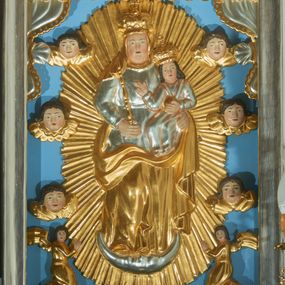 Zdjęcie nr 1: Obraz w kształcie stojącego prostokąta w drewnianej, srebrzonej ramie. W centrum kompozycji ukazana jest Matka Boska stojąca na półksiężycu z Dzieciątkiem Jezus na lewej ręce na tle złoconej, promienistej aureoli. Maria została ukazana w delikatnym kontrapoście z prawą nogą ugiętą w kolanie, w prawej dłoni trzyma berło. Ma szeroką, pełną twarz z dużym nosem oraz małymi ustami i oczami. Ubrana jest w srebrzoną suknię, przewiązaną w talii paskiem oraz złocony welon i złocony płaszcz osłaniający jej nogi i plecy. Dzieciątko siedzi zwrócone trzy czwarte w prawo, w lewej dłoni trzyma jabłko królewskie, a prawą czyni gest błogosławieństwa. Ma szeroką twarz o analogicznych rysach do twarzy Matki. Głowę Dzieciątka okalają długie, ciemne i bujne włosy. Maria i Dzieciątko mają na głowie założone pełne korony. W dolnej części kompozycji klęczą dwa aniołki, zwrócone do środka z twarzami w kierunku widza, ze złożonymi w geście modlitwy dłońmi. Po bokach obrazu umieszczonych jest też sześć uskrzydlonych główek anielskich skierowanych na wprost o pełnych twarzach i ciemnych, średniej długości włosach. W górnych narożach obrazu podwieszona jest srebrzona kotara ze złoconą bordiurą. Tło jednolite, błękitne. 
