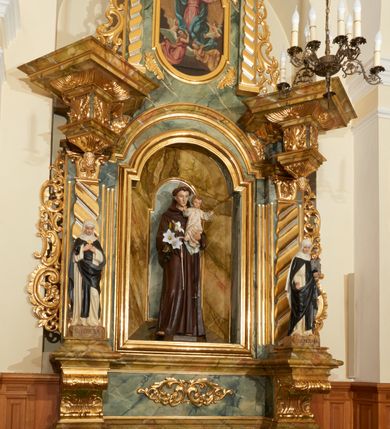 Zdjęcie nr 3: Ołtarz przyścienny, architektoniczny, jednoosiowy, jednokondygnacyjny ze zwieńczeniem. Mensa prostopadłościenna, w antepedium prostokątna, złocona rama. Prostokątna predella flankowana przed dwa wysunięte cokoły, na których ustawione są pilastry, wspierające przerwane belkowanie, zamknięte wydatnym, profilowanym gzymsem. Przed podporami ustawione są dwie figury świętych: po lewej stronie św. Teresy, a po prawej św. Kunegundy. W polu środkowym wnęka w kształcie stojącego prostokąta, zamkniętego łukiem nadwieszonym, w której umieszczona jest figura św. Antoniego Padewskiego na tle mniejszej płyciny o analogicznym kształcie. Imposty w partii fryzu ustawione są pod kątem, zdobione podwieszonymi od spodu szyszkami. Zwieńczenie w kształcie stojącego prostokąta, ujęte parą pilastrów, wspierających wyłamane belkowanie, zamknięte nad polem środkowym łukiem nadwieszonym. W polu obraz „Wniebowzięcie Najświętszej Marii Panny” w kształcie stojącego prostokąta od dołu i od góry zamkniętego łukiem nadwieszonym. Na szczycie zwieńczenia promienista gloria z monogramem maryjnym na tle obłoków. Podpory ustawione są na niskich bazach o trzonach dekorowanych płaską, skośnie oplatającą je szeroką wstęgą i o kapitelach korynckich. Boki nastawy i zwieńczenia zdobią uszaki formowane z ażurowej dekoracji rocaille’owej. Całość struktury ołtarza pokryta marmoryzacją zielono-niebieską; na cokole, fryzie, we wnęce i w zwieńczeniu cześciowo w kolorze jasnozielonym z jasnobrązowo-białym żyłkowaniem. Detale oraz profilowania pozłacane i posrebrzane. 
