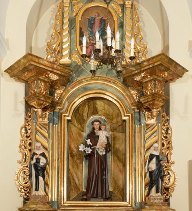 Zdjęcie nr 1: Ołtarz przyścienny, architektoniczny, jednoosiowy, jednokondygnacyjny ze zwieńczeniem. Mensa prostopadłościenna, w antepedium prostokątna, złocona rama. Prostokątna predella flankowana przed dwa wysunięte cokoły, na których ustawione są pilastry, wspierające przerwane belkowanie, zamknięte wydatnym, profilowanym gzymsem. Przed podporami ustawione są dwie figury świętych: po lewej stronie św. Teresy, a po prawej św. Kunegundy. W polu środkowym wnęka w kształcie stojącego prostokąta, zamkniętego łukiem nadwieszonym, w której umieszczona jest figura św. Antoniego Padewskiego na tle mniejszej płyciny o analogicznym kształcie. Imposty w partii fryzu ustawione są pod kątem, zdobione podwieszonymi od spodu szyszkami. Zwieńczenie w kształcie stojącego prostokąta, ujęte parą pilastrów, wspierających wyłamane belkowanie, zamknięte nad polem środkowym łukiem nadwieszonym. W polu obraz „Wniebowzięcie Najświętszej Marii Panny” w kształcie stojącego prostokąta od dołu i od góry zamkniętego łukiem nadwieszonym. Na szczycie zwieńczenia promienista gloria z monogramem maryjnym na tle obłoków. Podpory ustawione są na niskich bazach o trzonach dekorowanych płaską, skośnie oplatającą je szeroką wstęgą i o kapitelach korynckich. Boki nastawy i zwieńczenia zdobią uszaki formowane z ażurowej dekoracji rocaille’owej. Całość struktury ołtarza pokryta marmoryzacją zielono-niebieską; na cokole, fryzie, we wnęce i w zwieńczeniu cześciowo w kolorze jasnozielonym z jasnobrązowo-białym żyłkowaniem. Detale oraz profilowania pozłacane i posrebrzane. 
