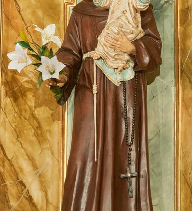 Zdjęcie nr 1: Rzeźba wolnostojąca z przedstawieniem św. Antoniego Padewskiego z Dzieciątkiem Jezus, ustawiona na cokole. Święty został ukazany w pozycji stojącej, w delikatnym kontrapoście z prawą nogą ugiętą w kolanie. Na lewej ręce trzyma Dzieciątko, a w prawej opuszczonej w dół gałązkę białej lilii (kwiaty sztuczne). Ma wąską twarz z długim nosem, drobne usta i małe oczy; na głowie tonsurę z silnie skręconych, krótkich włosów. Ubrany jest w brązowy habit franciszkański, przewiązany cingulum, a na lewym boku ma zawieszony długi, czarny różaniec; na stopach sandały. Cokół niski, prostopadłościenny o ściętych narożach, malowany w kolorze oliwkowozielonym. 