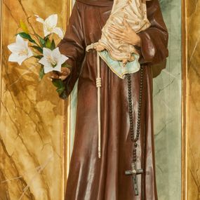 Zdjęcie nr 1: Rzeźba wolnostojąca z przedstawieniem św. Antoniego Padewskiego z Dzieciątkiem Jezus, ustawiona na cokole. Święty został ukazany w pozycji stojącej, w delikatnym kontrapoście z prawą nogą ugiętą w kolanie. Na lewej ręce trzyma Dzieciątko, a w prawej opuszczonej w dół gałązkę białej lilii (kwiaty sztuczne). Ma wąską twarz z długim nosem, drobne usta i małe oczy; na głowie tonsurę z silnie skręconych, krótkich włosów. Ubrany jest w brązowy habit franciszkański, przewiązany cingulum, a na lewym boku ma zawieszony długi, czarny różaniec; na stopach sandały. Cokół niski, prostopadłościenny o ściętych narożach, malowany w kolorze oliwkowozielonym. 