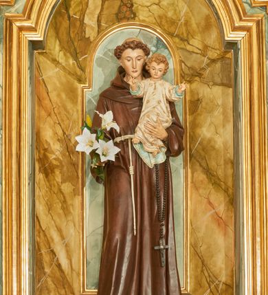 Zdjęcie nr 2: Rzeźba wolnostojąca z przedstawieniem św. Antoniego Padewskiego z Dzieciątkiem Jezus, ustawiona na cokole. Święty został ukazany w pozycji stojącej, w delikatnym kontrapoście z prawą nogą ugiętą w kolanie. Na lewej ręce trzyma Dzieciątko, a w prawej opuszczonej w dół gałązkę białej lilii (kwiaty sztuczne). Ma wąską twarz z długim nosem, drobne usta i małe oczy; na głowie tonsurę z silnie skręconych, krótkich włosów. Ubrany jest w brązowy habit franciszkański, przewiązany cingulum, a na lewym boku ma zawieszony długi, czarny różaniec; na stopach sandały. Cokół niski, prostopadłościenny o ściętych narożach, malowany w kolorze oliwkowozielonym. 