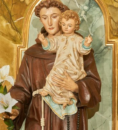 Zdjęcie nr 4: Rzeźba wolnostojąca z przedstawieniem św. Antoniego Padewskiego z Dzieciątkiem Jezus, ustawiona na cokole. Święty został ukazany w pozycji stojącej, w delikatnym kontrapoście z prawą nogą ugiętą w kolanie. Na lewej ręce trzyma Dzieciątko, a w prawej opuszczonej w dół gałązkę białej lilii (kwiaty sztuczne). Ma wąską twarz z długim nosem, drobne usta i małe oczy; na głowie tonsurę z silnie skręconych, krótkich włosów. Ubrany jest w brązowy habit franciszkański, przewiązany cingulum, a na lewym boku ma zawieszony długi, czarny różaniec; na stopach sandały. Cokół niski, prostopadłościenny o ściętych narożach, malowany w kolorze oliwkowozielonym. 