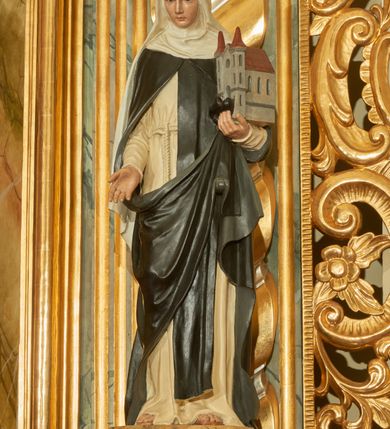 Zdjęcie nr 2: Rzeźba wolnostojąca z przedstawieniem św. Kunegundy, ustawiona na cokole. Święta została ukazana w pozycji stojącej, w delikatnym kontrapoście z prawą nogą ugiętą w kolanie. Zakonnica w lewej ręce trzyma model kościoła, a prawą opuszczoną w dół wyciąga przed siebie. Twarz owalna z długim i szerokim nosem, drobnymi ustami i dużymi oczami. Ubrana jest w biały habit, czarny szkaplerz, biały welon i podwikę oraz czarny płaszcz z prawą połą zarzuconą na lewe przedramię. Szaty drapowane są przeważnie w głębokie pionowe fałdy. Cokół prostopadłościenny o ściętych narożach, marmoryzowany, na ściance przedniej wyryty napis: „S(ANCTA) KUNEGUNDA”.