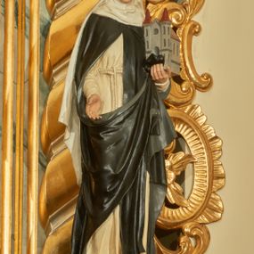 Zdjęcie nr 1: Rzeźba wolnostojąca z przedstawieniem św. Kunegundy, ustawiona na cokole. Święta została ukazana w pozycji stojącej, w delikatnym kontrapoście z prawą nogą ugiętą w kolanie. Zakonnica w lewej ręce trzyma model kościoła, a prawą opuszczoną w dół wyciąga przed siebie. Twarz owalna z długim i szerokim nosem, drobnymi ustami i dużymi oczami. Ubrana jest w biały habit, czarny szkaplerz, biały welon i podwikę oraz czarny płaszcz z prawą połą zarzuconą na lewe przedramię. Szaty drapowane są przeważnie w głębokie pionowe fałdy. Cokół prostopadłościenny o ściętych narożach, marmoryzowany, na ściance przedniej wyryty napis: „S(ANCTA) KUNEGUNDA”.