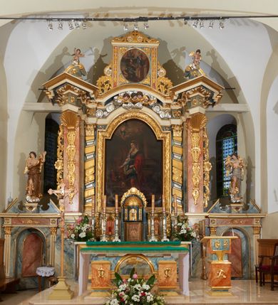 Zdjęcie nr 6: Obraz w prostokątnej, profilowanej ramie od góry zamkniętej łukiem nadwieszonym, przedstawiający św. Katarzynę Aleksandryjską, zwróconą trzy czwarte w prawo. Święta w prawej dłoni trzyma palmę męczeństwa, lewą wspiera się na rękojeści miecza. Twarz owalna o wyraźnych, linearnych rysach, dużych i brązowych oczach oraz długim nosie; na szyi sznur pereł, na uszach kolczyki. Ubrana jest w białą koszulę z długimi rękawami, niebieską tunikę ozdobioną złotą lamówką i przepasaną złotym pasem z ozdobną klamrą w formie rozety. Spod tuniki wystaje czerwona, długa suknia. Na lewe ramie ma narzucony czerwony płaszcz, luźno spływający na ziemię. Na głowie jest korona otwarta, od której z prawej strony spływa biały welon zdobiony w niebieskie paski. U stóp świętej, po lewej stronie obrazu leżą: korona zamknięta, topór i gałązka białej lilii. Święta przedstawiona jest na tle gładkiej kolumny na wysokim cokole, o który wsparte jest koło. Po przeciwnej stronie obrazu ukazani są trzej, pomniejszeni, dyskutujący filozofowie. Obok, również miniaturowa, scena przedstawiająca ścięcie św. Katarzyny. W oddali widoczne płonące koło. W górnej części obrazu są rozstępujące się niebiosa z aniołkiem trzymającym w dłoniach dwa wieńce; obok pary główek anielskich. Kolorystyka stonowana, ciepła, z przewagą brązów. Na odwrociu napis: „Obraz ten fundował ks(iądz) Michał Wawrzynowski Proboszcz w Nowym Targu Poświęciż był Jego / Em(inencja) Kardynał Książe Biskup Krakowski Albin Dunajeski / Kraków r(oku) p(ańskiego) 1892 Malował / Wł(adysław) Rossowski”.