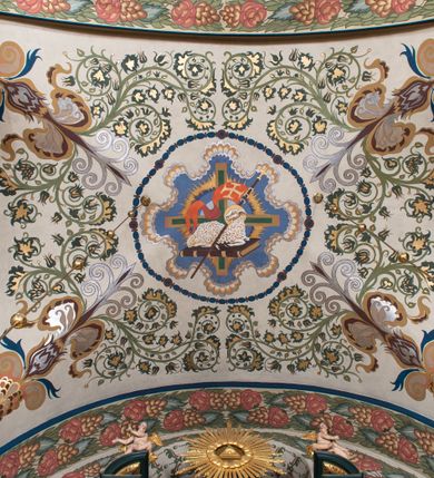 Zdjęcie nr 3: Dekoracja sklepienia nawy składa się z prostych symboli: kielicha z hostią, otwartej księgi z literami „A” i „Ω”, imienia MARIA i kotwicy. Zostały one wkomponowane w owalne medaliony w barwnej oprawie utworzonej z wieńców z żółtych i czerwonych kwiatów, złotych i zielonych wici akantów, ułożonych krzyżowo spiralnych, niebieskich ślimacznic i otaczających je stylizowanych zielonych liści akantu, między którymi przebijają się złote promienie. Owe fantazyjne kompozycje w nawie ukazane są na jasnym, kremowym tle wysklepek i niebieskich lunet i gurtów. Elementy konstrukcyjne szwów sklepiennych są podkreślone pasami z wici roślinnej. Sklepienie prezbiterium odróżnia się jaśniejszą kolorystyką. Elementy konstrukcyjne łuków podkreślają bujne czerwono-zielone kwiaty, wśród których rozpoznano piwonie. Taka sama bordiura zdobi ścianę za ołtarzem. Pośrodku umieszczono Baranka na zamkniętej księdze z chorągwią zmartwychwstania, na tle krzyża greckiego w glorii promienistej. Szwy sklepienne zaakcentowano kwiatami w układzie kandelabrowym, a wysklepki zielono-złotymi symetrycznie układającymi się wiciami roślinnymi. Na parapecie chóru muzycznego malarz przedstawił dwie sceny: „Stygmatyzacja św. Franciszka” i „Anioł grający na skrzypcach płaczącemu św. Franciszkowi”. 
