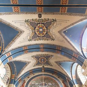 Zdjęcie nr 1: Dekoracja sklepienia nawy składa się z prostych symboli: kielicha z hostią, otwartej księgi z literami „A” i „Ω”, imienia MARIA i kotwicy. Zostały one wkomponowane w owalne medaliony w barwnej oprawie utworzonej z wieńców z żółtych i czerwonych kwiatów, złotych i zielonych wici akantów, ułożonych krzyżowo spiralnych, niebieskich ślimacznic i otaczających je stylizowanych zielonych liści akantu, między którymi przebijają się złote promienie. Owe fantazyjne kompozycje w nawie ukazane są na jasnym, kremowym tle wysklepek i niebieskich lunet i gurtów. Elementy konstrukcyjne szwów sklepiennych są podkreślone pasami z wici roślinnej. Sklepienie prezbiterium odróżnia się jaśniejszą kolorystyką. Elementy konstrukcyjne łuków podkreślają bujne czerwono-zielone kwiaty, wśród których rozpoznano piwonie. Taka sama bordiura zdobi ścianę za ołtarzem. Pośrodku umieszczono Baranka na zamkniętej księdze z chorągwią zmartwychwstania, na tle krzyża greckiego w glorii promienistej. Szwy sklepienne zaakcentowano kwiatami w układzie kandelabrowym, a wysklepki zielono-złotymi symetrycznie układającymi się wiciami roślinnymi. Na parapecie chóru muzycznego malarz przedstawił dwie sceny: „Stygmatyzacja św. Franciszka” i „Anioł grający na skrzypcach płaczącemu św. Franciszkowi”. 
