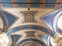 Zdjęcie nr 1: Dekoracja sklepienia nawy składa się z prostych symboli: kielicha z hostią, otwartej księgi z literami „A” i „Ω”, imienia MARIA i kotwicy. Zostały one wkomponowane w owalne medaliony w barwnej oprawie utworzonej z wieńców z żółtych i czerwonych kwiatów, złotych i zielonych wici akantów, ułożonych krzyżowo spiralnych, niebieskich ślimacznic i otaczających je stylizowanych zielonych liści akantu, między którymi przebijają się złote promienie. Owe fantazyjne kompozycje w nawie ukazane są na jasnym, kremowym tle wysklepek i niebieskich lunet i gurtów. Elementy konstrukcyjne szwów sklepiennych są podkreślone pasami z wici roślinnej. Sklepienie prezbiterium odróżnia się jaśniejszą kolorystyką. Elementy konstrukcyjne łuków podkreślają bujne czerwono-zielone kwiaty, wśród których rozpoznano piwonie. Taka sama bordiura zdobi ścianę za ołtarzem. Pośrodku umieszczono Baranka na zamkniętej księdze z chorągwią zmartwychwstania, na tle krzyża greckiego w glorii promienistej. Szwy sklepienne zaakcentowano kwiatami w układzie kandelabrowym, a wysklepki zielono-złotymi symetrycznie układającymi się wiciami roślinnymi. Na parapecie chóru muzycznego malarz przedstawił dwie sceny: „Stygmatyzacja św. Franciszka” i „Anioł grający na skrzypcach płaczącemu św. Franciszkowi”. 
