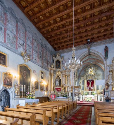 Zdjęcie nr 67: Kościół murowany z cegły, z użyciem zendrówki, na wysokim podmurowaniu z kamienia łupanego, jednonawowy, orientowany. 
Prezbiterium i nawa na planie prostokątów, nawa szersza i dłuższa od prezbiterium. Zakrystia na rzucie wydłużonego prostokąta przylega do wschodniej ściany prezbiterium, występując poza mury nawy. Prezbiterium od wschodu ujęte w narożach dwiema ukośnymi szkarpami, od południa jedną prostopadłą. Przy południowej ścianie nawy kruchta na planie kwadratu. Nawa w narożach ujęta szkarpami, od wschodu dwiema prostopadłymi, od zachodu ukośnymi. 
Prezbiterium dwuprzęsłowe, nakryte sklepieniem krzyżowo-żebrowym. Na zwornikach dwie tarcze z herbami Trzy Korony i Wieniawa. Zakrystia sklepiona kolebkowo. Nawa nakryta drewnianym stropem z kasetonami i rozetami. Kruchta sklepiona krzyżowo-żebrowo ze zwornikiem z tarczą z herbem Wieniawa. Otwór tęczowy w formie stojącego prostokąta zamkniętego łukiem ostrym. W zachodniej części nawy drewniany parapet chóru muzycznego wsparty na dwóch filarach. 
Fasada w jednej trzeciej wysokości odcięta kamiennym gzymsem kapnikowym, zakończona jodełkowym fryzem w partii muru, zwieńczona trójkątnym szczytem. Mur dekorowany zendrówką ułożoną „w zęby”, w partii szczytu w układzie rombowym. Na osi kamienny ostrołukowy portal o schodkowym nadprożu, dekorowanym krzyżującym się laskowaniem; węgary gładkie w jednej trzeciej wysokości przechodzące w piramidki i profilowanie powyżej. Nad portalem kamienna kwadratowa tablica, ujęta kamiennym obramieniem z tarczą z herbem Wieniawa. Ponad nią, na osi okulus w kamiennym obramieniu. 
Elewacje północna i południowa w części nawy w jednej trzeciej wysokości przedzielone kamiennym gzymsem kapnikowym, na zakończeniu ścian z gzymsem wieńczącym. Mur dekorowany zendrówką w układzie rombowym. Na elewacji południowej cztery okna w formie wydłużonego, stojącego prostokąta zamkniętego łukiem ostrym, w kamiennych obramieniach, podzielone laskowaniem. Południowa ściana prezbiterium zakończona gzymsem wieńczącym, w górnej części muru dekorowana zendrówką ułożoną „w zęby”. 
Szkarpy opinające nawę uskokowe, zwężające się ku górze, nakryte daszkami pulpitowymi. Szkarpy opinające prezbiterium nakryte daszkami pulpitowymi, podzielone gzymsami kapnikowymi. 
Kruchta od strony wschodniej i zachodniej podzielona kamiennym gzymsem kapnikowym, od południa zakończona gzymsem wieńczącym. Na ścianie południowej kruchty kamienny, ostrołukowy portal, o schodkowym nadprożu, dekorowanym krzyżującym się laskowaniem; węgary gładkie, w jednej trzeciej wysokości przechodzące w piramidki i profilowanie powyżej. Nad portalem kamienna tarcza z herbem Wieniawa. 
Elewacja wschodnia zwieńczona trójkątnym szczytem, w którego partii mur dekorowany jest zendrówką w układzie rombowym. Na osi okno w formie wydłużonego, stojącego prostokąta zamkniętego łukiem ostrym, w kamiennym obramieniu, zamurowane w trzech piątych wysokości, zakończone daszkiem pulpitowym. W dolnej części okna znajduje się ogrójec. 
Nawa i prezbiterium nakryte osobnymi blaszanymi dachami dwuspadowymi, kruchta i zakrystia pulpitowymi. Nad nawą blaszana wieżyczka na sygnaturkę z latarnią i hełmem baniastym.





