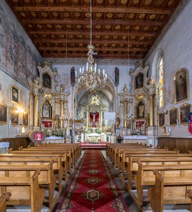 Zdjęcie nr 69: Kościół murowany z cegły, z użyciem zendrówki, na wysokim podmurowaniu z kamienia łupanego, jednonawowy, orientowany. 
Prezbiterium i nawa na planie prostokątów, nawa szersza i dłuższa od prezbiterium. Zakrystia na rzucie wydłużonego prostokąta przylega do wschodniej ściany prezbiterium, występując poza mury nawy. Prezbiterium od wschodu ujęte w narożach dwiema ukośnymi szkarpami, od południa jedną prostopadłą. Przy południowej ścianie nawy kruchta na planie kwadratu. Nawa w narożach ujęta szkarpami, od wschodu dwiema prostopadłymi, od zachodu ukośnymi. 
Prezbiterium dwuprzęsłowe, nakryte sklepieniem krzyżowo-żebrowym. Na zwornikach dwie tarcze z herbami Trzy Korony i Wieniawa. Zakrystia sklepiona kolebkowo. Nawa nakryta drewnianym stropem z kasetonami i rozetami. Kruchta sklepiona krzyżowo-żebrowo ze zwornikiem z tarczą z herbem Wieniawa. Otwór tęczowy w formie stojącego prostokąta zamkniętego łukiem ostrym. W zachodniej części nawy drewniany parapet chóru muzycznego wsparty na dwóch filarach. 
Fasada w jednej trzeciej wysokości odcięta kamiennym gzymsem kapnikowym, zakończona jodełkowym fryzem w partii muru, zwieńczona trójkątnym szczytem. Mur dekorowany zendrówką ułożoną „w zęby”, w partii szczytu w układzie rombowym. Na osi kamienny ostrołukowy portal o schodkowym nadprożu, dekorowanym krzyżującym się laskowaniem; węgary gładkie w jednej trzeciej wysokości przechodzące w piramidki i profilowanie powyżej. Nad portalem kamienna kwadratowa tablica, ujęta kamiennym obramieniem z tarczą z herbem Wieniawa. Ponad nią, na osi okulus w kamiennym obramieniu. 
Elewacje północna i południowa w części nawy w jednej trzeciej wysokości przedzielone kamiennym gzymsem kapnikowym, na zakończeniu ścian z gzymsem wieńczącym. Mur dekorowany zendrówką w układzie rombowym. Na elewacji południowej cztery okna w formie wydłużonego, stojącego prostokąta zamkniętego łukiem ostrym, w kamiennych obramieniach, podzielone laskowaniem. Południowa ściana prezbiterium zakończona gzymsem wieńczącym, w górnej części muru dekorowana zendrówką ułożoną „w zęby”. 
Szkarpy opinające nawę uskokowe, zwężające się ku górze, nakryte daszkami pulpitowymi. Szkarpy opinające prezbiterium nakryte daszkami pulpitowymi, podzielone gzymsami kapnikowymi. 
Kruchta od strony wschodniej i zachodniej podzielona kamiennym gzymsem kapnikowym, od południa zakończona gzymsem wieńczącym. Na ścianie południowej kruchty kamienny, ostrołukowy portal, o schodkowym nadprożu, dekorowanym krzyżującym się laskowaniem; węgary gładkie, w jednej trzeciej wysokości przechodzące w piramidki i profilowanie powyżej. Nad portalem kamienna tarcza z herbem Wieniawa. 
Elewacja wschodnia zwieńczona trójkątnym szczytem, w którego partii mur dekorowany jest zendrówką w układzie rombowym. Na osi okno w formie wydłużonego, stojącego prostokąta zamkniętego łukiem ostrym, w kamiennym obramieniu, zamurowane w trzech piątych wysokości, zakończone daszkiem pulpitowym. W dolnej części okna znajduje się ogrójec. 
Nawa i prezbiterium nakryte osobnymi blaszanymi dachami dwuspadowymi, kruchta i zakrystia pulpitowymi. Nad nawą blaszana wieżyczka na sygnaturkę z latarnią i hełmem baniastym.





