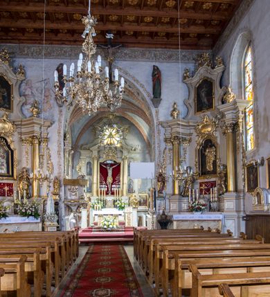 Zdjęcie nr 66: Kościół murowany z cegły, z użyciem zendrówki, na wysokim podmurowaniu z kamienia łupanego, jednonawowy, orientowany. 
Prezbiterium i nawa na planie prostokątów, nawa szersza i dłuższa od prezbiterium. Zakrystia na rzucie wydłużonego prostokąta przylega do wschodniej ściany prezbiterium, występując poza mury nawy. Prezbiterium od wschodu ujęte w narożach dwiema ukośnymi szkarpami, od południa jedną prostopadłą. Przy południowej ścianie nawy kruchta na planie kwadratu. Nawa w narożach ujęta szkarpami, od wschodu dwiema prostopadłymi, od zachodu ukośnymi. 
Prezbiterium dwuprzęsłowe, nakryte sklepieniem krzyżowo-żebrowym. Na zwornikach dwie tarcze z herbami Trzy Korony i Wieniawa. Zakrystia sklepiona kolebkowo. Nawa nakryta drewnianym stropem z kasetonami i rozetami. Kruchta sklepiona krzyżowo-żebrowo ze zwornikiem z tarczą z herbem Wieniawa. Otwór tęczowy w formie stojącego prostokąta zamkniętego łukiem ostrym. W zachodniej części nawy drewniany parapet chóru muzycznego wsparty na dwóch filarach. 
Fasada w jednej trzeciej wysokości odcięta kamiennym gzymsem kapnikowym, zakończona jodełkowym fryzem w partii muru, zwieńczona trójkątnym szczytem. Mur dekorowany zendrówką ułożoną „w zęby”, w partii szczytu w układzie rombowym. Na osi kamienny ostrołukowy portal o schodkowym nadprożu, dekorowanym krzyżującym się laskowaniem; węgary gładkie w jednej trzeciej wysokości przechodzące w piramidki i profilowanie powyżej. Nad portalem kamienna kwadratowa tablica, ujęta kamiennym obramieniem z tarczą z herbem Wieniawa. Ponad nią, na osi okulus w kamiennym obramieniu. 
Elewacje północna i południowa w części nawy w jednej trzeciej wysokości przedzielone kamiennym gzymsem kapnikowym, na zakończeniu ścian z gzymsem wieńczącym. Mur dekorowany zendrówką w układzie rombowym. Na elewacji południowej cztery okna w formie wydłużonego, stojącego prostokąta zamkniętego łukiem ostrym, w kamiennych obramieniach, podzielone laskowaniem. Południowa ściana prezbiterium zakończona gzymsem wieńczącym, w górnej części muru dekorowana zendrówką ułożoną „w zęby”. 
Szkarpy opinające nawę uskokowe, zwężające się ku górze, nakryte daszkami pulpitowymi. Szkarpy opinające prezbiterium nakryte daszkami pulpitowymi, podzielone gzymsami kapnikowymi. 
Kruchta od strony wschodniej i zachodniej podzielona kamiennym gzymsem kapnikowym, od południa zakończona gzymsem wieńczącym. Na ścianie południowej kruchty kamienny, ostrołukowy portal, o schodkowym nadprożu, dekorowanym krzyżującym się laskowaniem; węgary gładkie, w jednej trzeciej wysokości przechodzące w piramidki i profilowanie powyżej. Nad portalem kamienna tarcza z herbem Wieniawa. 
Elewacja wschodnia zwieńczona trójkątnym szczytem, w którego partii mur dekorowany jest zendrówką w układzie rombowym. Na osi okno w formie wydłużonego, stojącego prostokąta zamkniętego łukiem ostrym, w kamiennym obramieniu, zamurowane w trzech piątych wysokości, zakończone daszkiem pulpitowym. W dolnej części okna znajduje się ogrójec. 
Nawa i prezbiterium nakryte osobnymi blaszanymi dachami dwuspadowymi, kruchta i zakrystia pulpitowymi. Nad nawą blaszana wieżyczka na sygnaturkę z latarnią i hełmem baniastym.





