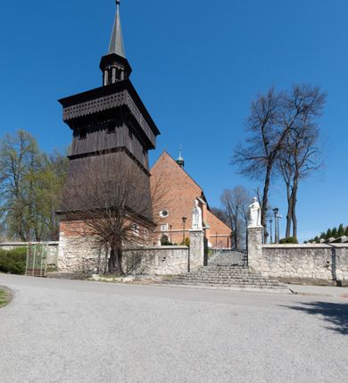 Zdjęcie nr 42: Kościół murowany z cegły, z użyciem zendrówki, na wysokim podmurowaniu z kamienia łupanego, jednonawowy, orientowany. 
Prezbiterium i nawa na planie prostokątów, nawa szersza i dłuższa od prezbiterium. Zakrystia na rzucie wydłużonego prostokąta przylega do wschodniej ściany prezbiterium, występując poza mury nawy. Prezbiterium od wschodu ujęte w narożach dwiema ukośnymi szkarpami, od południa jedną prostopadłą. Przy południowej ścianie nawy kruchta na planie kwadratu. Nawa w narożach ujęta szkarpami, od wschodu dwiema prostopadłymi, od zachodu ukośnymi. 
Prezbiterium dwuprzęsłowe, nakryte sklepieniem krzyżowo-żebrowym. Na zwornikach dwie tarcze z herbami Trzy Korony i Wieniawa. Zakrystia sklepiona kolebkowo. Nawa nakryta drewnianym stropem z kasetonami i rozetami. Kruchta sklepiona krzyżowo-żebrowo ze zwornikiem z tarczą z herbem Wieniawa. Otwór tęczowy w formie stojącego prostokąta zamkniętego łukiem ostrym. W zachodniej części nawy drewniany parapet chóru muzycznego wsparty na dwóch filarach. 
Fasada w jednej trzeciej wysokości odcięta kamiennym gzymsem kapnikowym, zakończona jodełkowym fryzem w partii muru, zwieńczona trójkątnym szczytem. Mur dekorowany zendrówką ułożoną „w zęby”, w partii szczytu w układzie rombowym. Na osi kamienny ostrołukowy portal o schodkowym nadprożu, dekorowanym krzyżującym się laskowaniem; węgary gładkie w jednej trzeciej wysokości przechodzące w piramidki i profilowanie powyżej. Nad portalem kamienna kwadratowa tablica, ujęta kamiennym obramieniem z tarczą z herbem Wieniawa. Ponad nią, na osi okulus w kamiennym obramieniu. 
Elewacje północna i południowa w części nawy w jednej trzeciej wysokości przedzielone kamiennym gzymsem kapnikowym, na zakończeniu ścian z gzymsem wieńczącym. Mur dekorowany zendrówką w układzie rombowym. Na elewacji południowej cztery okna w formie wydłużonego, stojącego prostokąta zamkniętego łukiem ostrym, w kamiennych obramieniach, podzielone laskowaniem. Południowa ściana prezbiterium zakończona gzymsem wieńczącym, w górnej części muru dekorowana zendrówką ułożoną „w zęby”. 
Szkarpy opinające nawę uskokowe, zwężające się ku górze, nakryte daszkami pulpitowymi. Szkarpy opinające prezbiterium nakryte daszkami pulpitowymi, podzielone gzymsami kapnikowymi. 
Kruchta od strony wschodniej i zachodniej podzielona kamiennym gzymsem kapnikowym, od południa zakończona gzymsem wieńczącym. Na ścianie południowej kruchty kamienny, ostrołukowy portal, o schodkowym nadprożu, dekorowanym krzyżującym się laskowaniem; węgary gładkie, w jednej trzeciej wysokości przechodzące w piramidki i profilowanie powyżej. Nad portalem kamienna tarcza z herbem Wieniawa. 
Elewacja wschodnia zwieńczona trójkątnym szczytem, w którego partii mur dekorowany jest zendrówką w układzie rombowym. Na osi okno w formie wydłużonego, stojącego prostokąta zamkniętego łukiem ostrym, w kamiennym obramieniu, zamurowane w trzech piątych wysokości, zakończone daszkiem pulpitowym. W dolnej części okna znajduje się ogrójec. 
Nawa i prezbiterium nakryte osobnymi blaszanymi dachami dwuspadowymi, kruchta i zakrystia pulpitowymi. Nad nawą blaszana wieżyczka na sygnaturkę z latarnią i hełmem baniastym.





