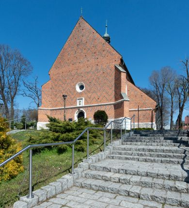 Zdjęcie nr 36: Kościół murowany z cegły, z użyciem zendrówki, na wysokim podmurowaniu z kamienia łupanego, jednonawowy, orientowany. 
Prezbiterium i nawa na planie prostokątów, nawa szersza i dłuższa od prezbiterium. Zakrystia na rzucie wydłużonego prostokąta przylega do wschodniej ściany prezbiterium, występując poza mury nawy. Prezbiterium od wschodu ujęte w narożach dwiema ukośnymi szkarpami, od południa jedną prostopadłą. Przy południowej ścianie nawy kruchta na planie kwadratu. Nawa w narożach ujęta szkarpami, od wschodu dwiema prostopadłymi, od zachodu ukośnymi. 
Prezbiterium dwuprzęsłowe, nakryte sklepieniem krzyżowo-żebrowym. Na zwornikach dwie tarcze z herbami Trzy Korony i Wieniawa. Zakrystia sklepiona kolebkowo. Nawa nakryta drewnianym stropem z kasetonami i rozetami. Kruchta sklepiona krzyżowo-żebrowo ze zwornikiem z tarczą z herbem Wieniawa. Otwór tęczowy w formie stojącego prostokąta zamkniętego łukiem ostrym. W zachodniej części nawy drewniany parapet chóru muzycznego wsparty na dwóch filarach. 
Fasada w jednej trzeciej wysokości odcięta kamiennym gzymsem kapnikowym, zakończona jodełkowym fryzem w partii muru, zwieńczona trójkątnym szczytem. Mur dekorowany zendrówką ułożoną „w zęby”, w partii szczytu w układzie rombowym. Na osi kamienny ostrołukowy portal o schodkowym nadprożu, dekorowanym krzyżującym się laskowaniem; węgary gładkie w jednej trzeciej wysokości przechodzące w piramidki i profilowanie powyżej. Nad portalem kamienna kwadratowa tablica, ujęta kamiennym obramieniem z tarczą z herbem Wieniawa. Ponad nią, na osi okulus w kamiennym obramieniu. 
Elewacje północna i południowa w części nawy w jednej trzeciej wysokości przedzielone kamiennym gzymsem kapnikowym, na zakończeniu ścian z gzymsem wieńczącym. Mur dekorowany zendrówką w układzie rombowym. Na elewacji południowej cztery okna w formie wydłużonego, stojącego prostokąta zamkniętego łukiem ostrym, w kamiennych obramieniach, podzielone laskowaniem. Południowa ściana prezbiterium zakończona gzymsem wieńczącym, w górnej części muru dekorowana zendrówką ułożoną „w zęby”. 
Szkarpy opinające nawę uskokowe, zwężające się ku górze, nakryte daszkami pulpitowymi. Szkarpy opinające prezbiterium nakryte daszkami pulpitowymi, podzielone gzymsami kapnikowymi. 
Kruchta od strony wschodniej i zachodniej podzielona kamiennym gzymsem kapnikowym, od południa zakończona gzymsem wieńczącym. Na ścianie południowej kruchty kamienny, ostrołukowy portal, o schodkowym nadprożu, dekorowanym krzyżującym się laskowaniem; węgary gładkie, w jednej trzeciej wysokości przechodzące w piramidki i profilowanie powyżej. Nad portalem kamienna tarcza z herbem Wieniawa. 
Elewacja wschodnia zwieńczona trójkątnym szczytem, w którego partii mur dekorowany jest zendrówką w układzie rombowym. Na osi okno w formie wydłużonego, stojącego prostokąta zamkniętego łukiem ostrym, w kamiennym obramieniu, zamurowane w trzech piątych wysokości, zakończone daszkiem pulpitowym. W dolnej części okna znajduje się ogrójec. 
Nawa i prezbiterium nakryte osobnymi blaszanymi dachami dwuspadowymi, kruchta i zakrystia pulpitowymi. Nad nawą blaszana wieżyczka na sygnaturkę z latarnią i hełmem baniastym.





