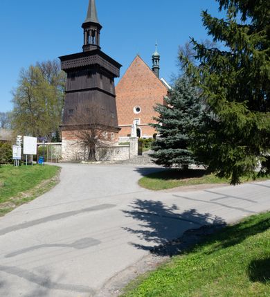 Zdjęcie nr 43: Kościół murowany z cegły, z użyciem zendrówki, na wysokim podmurowaniu z kamienia łupanego, jednonawowy, orientowany. 
Prezbiterium i nawa na planie prostokątów, nawa szersza i dłuższa od prezbiterium. Zakrystia na rzucie wydłużonego prostokąta przylega do wschodniej ściany prezbiterium, występując poza mury nawy. Prezbiterium od wschodu ujęte w narożach dwiema ukośnymi szkarpami, od południa jedną prostopadłą. Przy południowej ścianie nawy kruchta na planie kwadratu. Nawa w narożach ujęta szkarpami, od wschodu dwiema prostopadłymi, od zachodu ukośnymi. 
Prezbiterium dwuprzęsłowe, nakryte sklepieniem krzyżowo-żebrowym. Na zwornikach dwie tarcze z herbami Trzy Korony i Wieniawa. Zakrystia sklepiona kolebkowo. Nawa nakryta drewnianym stropem z kasetonami i rozetami. Kruchta sklepiona krzyżowo-żebrowo ze zwornikiem z tarczą z herbem Wieniawa. Otwór tęczowy w formie stojącego prostokąta zamkniętego łukiem ostrym. W zachodniej części nawy drewniany parapet chóru muzycznego wsparty na dwóch filarach. 
Fasada w jednej trzeciej wysokości odcięta kamiennym gzymsem kapnikowym, zakończona jodełkowym fryzem w partii muru, zwieńczona trójkątnym szczytem. Mur dekorowany zendrówką ułożoną „w zęby”, w partii szczytu w układzie rombowym. Na osi kamienny ostrołukowy portal o schodkowym nadprożu, dekorowanym krzyżującym się laskowaniem; węgary gładkie w jednej trzeciej wysokości przechodzące w piramidki i profilowanie powyżej. Nad portalem kamienna kwadratowa tablica, ujęta kamiennym obramieniem z tarczą z herbem Wieniawa. Ponad nią, na osi okulus w kamiennym obramieniu. 
Elewacje północna i południowa w części nawy w jednej trzeciej wysokości przedzielone kamiennym gzymsem kapnikowym, na zakończeniu ścian z gzymsem wieńczącym. Mur dekorowany zendrówką w układzie rombowym. Na elewacji południowej cztery okna w formie wydłużonego, stojącego prostokąta zamkniętego łukiem ostrym, w kamiennych obramieniach, podzielone laskowaniem. Południowa ściana prezbiterium zakończona gzymsem wieńczącym, w górnej części muru dekorowana zendrówką ułożoną „w zęby”. 
Szkarpy opinające nawę uskokowe, zwężające się ku górze, nakryte daszkami pulpitowymi. Szkarpy opinające prezbiterium nakryte daszkami pulpitowymi, podzielone gzymsami kapnikowymi. 
Kruchta od strony wschodniej i zachodniej podzielona kamiennym gzymsem kapnikowym, od południa zakończona gzymsem wieńczącym. Na ścianie południowej kruchty kamienny, ostrołukowy portal, o schodkowym nadprożu, dekorowanym krzyżującym się laskowaniem; węgary gładkie, w jednej trzeciej wysokości przechodzące w piramidki i profilowanie powyżej. Nad portalem kamienna tarcza z herbem Wieniawa. 
Elewacja wschodnia zwieńczona trójkątnym szczytem, w którego partii mur dekorowany jest zendrówką w układzie rombowym. Na osi okno w formie wydłużonego, stojącego prostokąta zamkniętego łukiem ostrym, w kamiennym obramieniu, zamurowane w trzech piątych wysokości, zakończone daszkiem pulpitowym. W dolnej części okna znajduje się ogrójec. 
Nawa i prezbiterium nakryte osobnymi blaszanymi dachami dwuspadowymi, kruchta i zakrystia pulpitowymi. Nad nawą blaszana wieżyczka na sygnaturkę z latarnią i hełmem baniastym.





