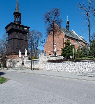 Zdjęcie nr 41: Kościół murowany z cegły, z użyciem zendrówki, na wysokim podmurowaniu z kamienia łupanego, jednonawowy, orientowany. 
Prezbiterium i nawa na planie prostokątów, nawa szersza i dłuższa od prezbiterium. Zakrystia na rzucie wydłużonego prostokąta przylega do wschodniej ściany prezbiterium, występując poza mury nawy. Prezbiterium od wschodu ujęte w narożach dwiema ukośnymi szkarpami, od południa jedną prostopadłą. Przy południowej ścianie nawy kruchta na planie kwadratu. Nawa w narożach ujęta szkarpami, od wschodu dwiema prostopadłymi, od zachodu ukośnymi. 
Prezbiterium dwuprzęsłowe, nakryte sklepieniem krzyżowo-żebrowym. Na zwornikach dwie tarcze z herbami Trzy Korony i Wieniawa. Zakrystia sklepiona kolebkowo. Nawa nakryta drewnianym stropem z kasetonami i rozetami. Kruchta sklepiona krzyżowo-żebrowo ze zwornikiem z tarczą z herbem Wieniawa. Otwór tęczowy w formie stojącego prostokąta zamkniętego łukiem ostrym. W zachodniej części nawy drewniany parapet chóru muzycznego wsparty na dwóch filarach. 
Fasada w jednej trzeciej wysokości odcięta kamiennym gzymsem kapnikowym, zakończona jodełkowym fryzem w partii muru, zwieńczona trójkątnym szczytem. Mur dekorowany zendrówką ułożoną „w zęby”, w partii szczytu w układzie rombowym. Na osi kamienny ostrołukowy portal o schodkowym nadprożu, dekorowanym krzyżującym się laskowaniem; węgary gładkie w jednej trzeciej wysokości przechodzące w piramidki i profilowanie powyżej. Nad portalem kamienna kwadratowa tablica, ujęta kamiennym obramieniem z tarczą z herbem Wieniawa. Ponad nią, na osi okulus w kamiennym obramieniu. 
Elewacje północna i południowa w części nawy w jednej trzeciej wysokości przedzielone kamiennym gzymsem kapnikowym, na zakończeniu ścian z gzymsem wieńczącym. Mur dekorowany zendrówką w układzie rombowym. Na elewacji południowej cztery okna w formie wydłużonego, stojącego prostokąta zamkniętego łukiem ostrym, w kamiennych obramieniach, podzielone laskowaniem. Południowa ściana prezbiterium zakończona gzymsem wieńczącym, w górnej części muru dekorowana zendrówką ułożoną „w zęby”. 
Szkarpy opinające nawę uskokowe, zwężające się ku górze, nakryte daszkami pulpitowymi. Szkarpy opinające prezbiterium nakryte daszkami pulpitowymi, podzielone gzymsami kapnikowymi. 
Kruchta od strony wschodniej i zachodniej podzielona kamiennym gzymsem kapnikowym, od południa zakończona gzymsem wieńczącym. Na ścianie południowej kruchty kamienny, ostrołukowy portal, o schodkowym nadprożu, dekorowanym krzyżującym się laskowaniem; węgary gładkie, w jednej trzeciej wysokości przechodzące w piramidki i profilowanie powyżej. Nad portalem kamienna tarcza z herbem Wieniawa. 
Elewacja wschodnia zwieńczona trójkątnym szczytem, w którego partii mur dekorowany jest zendrówką w układzie rombowym. Na osi okno w formie wydłużonego, stojącego prostokąta zamkniętego łukiem ostrym, w kamiennym obramieniu, zamurowane w trzech piątych wysokości, zakończone daszkiem pulpitowym. W dolnej części okna znajduje się ogrójec. 
Nawa i prezbiterium nakryte osobnymi blaszanymi dachami dwuspadowymi, kruchta i zakrystia pulpitowymi. Nad nawą blaszana wieżyczka na sygnaturkę z latarnią i hełmem baniastym.





