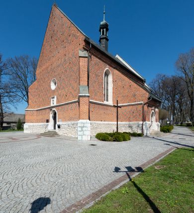 Zdjęcie nr 2: Kościół murowany z cegły, z użyciem zendrówki, na wysokim podmurowaniu z kamienia łupanego, jednonawowy, orientowany. 
Prezbiterium i nawa na planie prostokątów, nawa szersza i dłuższa od prezbiterium. Zakrystia na rzucie wydłużonego prostokąta przylega do wschodniej ściany prezbiterium, występując poza mury nawy. Prezbiterium od wschodu ujęte w narożach dwiema ukośnymi szkarpami, od południa jedną prostopadłą. Przy południowej ścianie nawy kruchta na planie kwadratu. Nawa w narożach ujęta szkarpami, od wschodu dwiema prostopadłymi, od zachodu ukośnymi. 
Prezbiterium dwuprzęsłowe, nakryte sklepieniem krzyżowo-żebrowym. Na zwornikach dwie tarcze z herbami Trzy Korony i Wieniawa. Zakrystia sklepiona kolebkowo. Nawa nakryta drewnianym stropem z kasetonami i rozetami. Kruchta sklepiona krzyżowo-żebrowo ze zwornikiem z tarczą z herbem Wieniawa. Otwór tęczowy w formie stojącego prostokąta zamkniętego łukiem ostrym. W zachodniej części nawy drewniany parapet chóru muzycznego wsparty na dwóch filarach. 
Fasada w jednej trzeciej wysokości odcięta kamiennym gzymsem kapnikowym, zakończona jodełkowym fryzem w partii muru, zwieńczona trójkątnym szczytem. Mur dekorowany zendrówką ułożoną „w zęby”, w partii szczytu w układzie rombowym. Na osi kamienny ostrołukowy portal o schodkowym nadprożu, dekorowanym krzyżującym się laskowaniem; węgary gładkie w jednej trzeciej wysokości przechodzące w piramidki i profilowanie powyżej. Nad portalem kamienna kwadratowa tablica, ujęta kamiennym obramieniem z tarczą z herbem Wieniawa. Ponad nią, na osi okulus w kamiennym obramieniu. 
Elewacje północna i południowa w części nawy w jednej trzeciej wysokości przedzielone kamiennym gzymsem kapnikowym, na zakończeniu ścian z gzymsem wieńczącym. Mur dekorowany zendrówką w układzie rombowym. Na elewacji południowej cztery okna w formie wydłużonego, stojącego prostokąta zamkniętego łukiem ostrym, w kamiennych obramieniach, podzielone laskowaniem. Południowa ściana prezbiterium zakończona gzymsem wieńczącym, w górnej części muru dekorowana zendrówką ułożoną „w zęby”. 
Szkarpy opinające nawę uskokowe, zwężające się ku górze, nakryte daszkami pulpitowymi. Szkarpy opinające prezbiterium nakryte daszkami pulpitowymi, podzielone gzymsami kapnikowymi. 
Kruchta od strony wschodniej i zachodniej podzielona kamiennym gzymsem kapnikowym, od południa zakończona gzymsem wieńczącym. Na ścianie południowej kruchty kamienny, ostrołukowy portal, o schodkowym nadprożu, dekorowanym krzyżującym się laskowaniem; węgary gładkie, w jednej trzeciej wysokości przechodzące w piramidki i profilowanie powyżej. Nad portalem kamienna tarcza z herbem Wieniawa. 
Elewacja wschodnia zwieńczona trójkątnym szczytem, w którego partii mur dekorowany jest zendrówką w układzie rombowym. Na osi okno w formie wydłużonego, stojącego prostokąta zamkniętego łukiem ostrym, w kamiennym obramieniu, zamurowane w trzech piątych wysokości, zakończone daszkiem pulpitowym. W dolnej części okna znajduje się ogrójec. 
Nawa i prezbiterium nakryte osobnymi blaszanymi dachami dwuspadowymi, kruchta i zakrystia pulpitowymi. Nad nawą blaszana wieżyczka na sygnaturkę z latarnią i hełmem baniastym.





